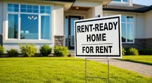 A house with a sign in front that reads 'Rent-Ready Home For Rent' in a suburban neighborhood with well-maintained lawn and large windows.