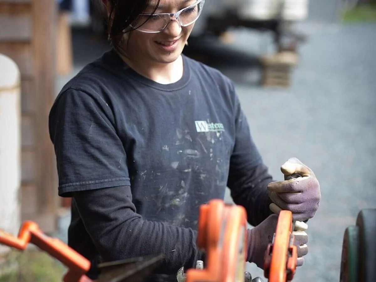A woman wearing glasses and a black shirt working with clippers outside, possibly gardening or doing yard work.