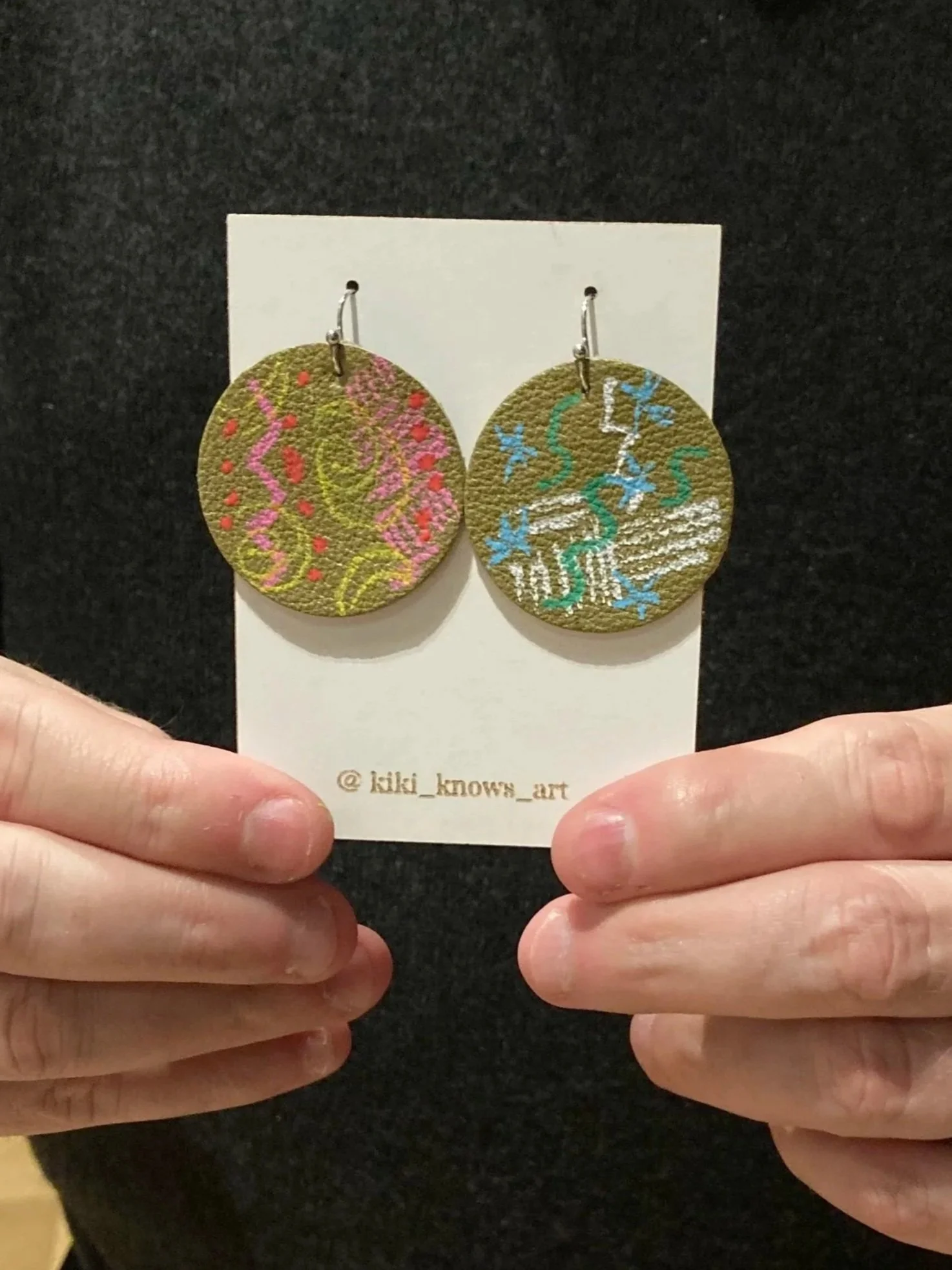 A pair of circular earrings with colorful, swirling designs, made at a Kiki Knows Art jewelry workshop.