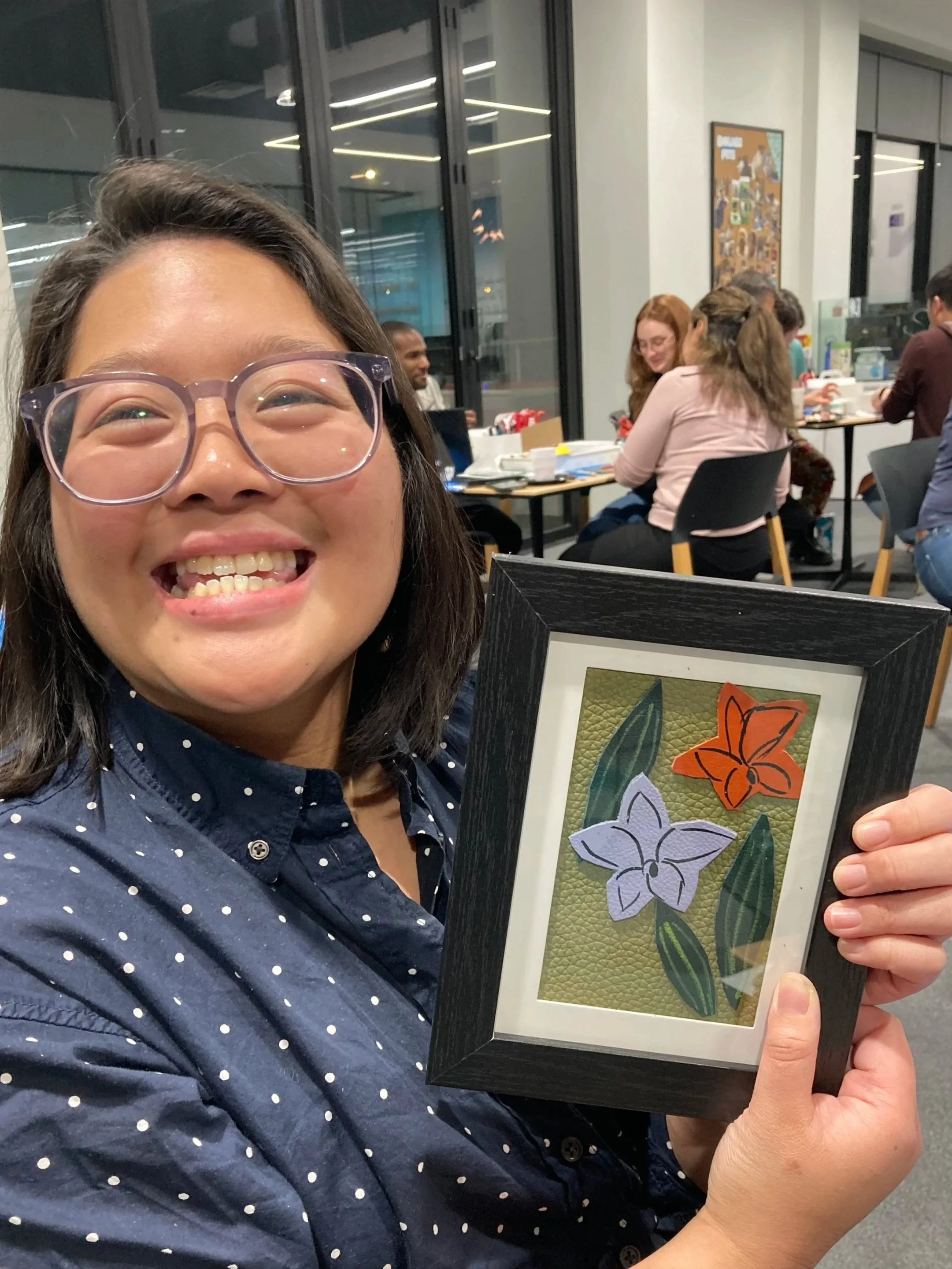 A woman smiling and holding her leather craft creation at a Kiki Knows Art Workshop.