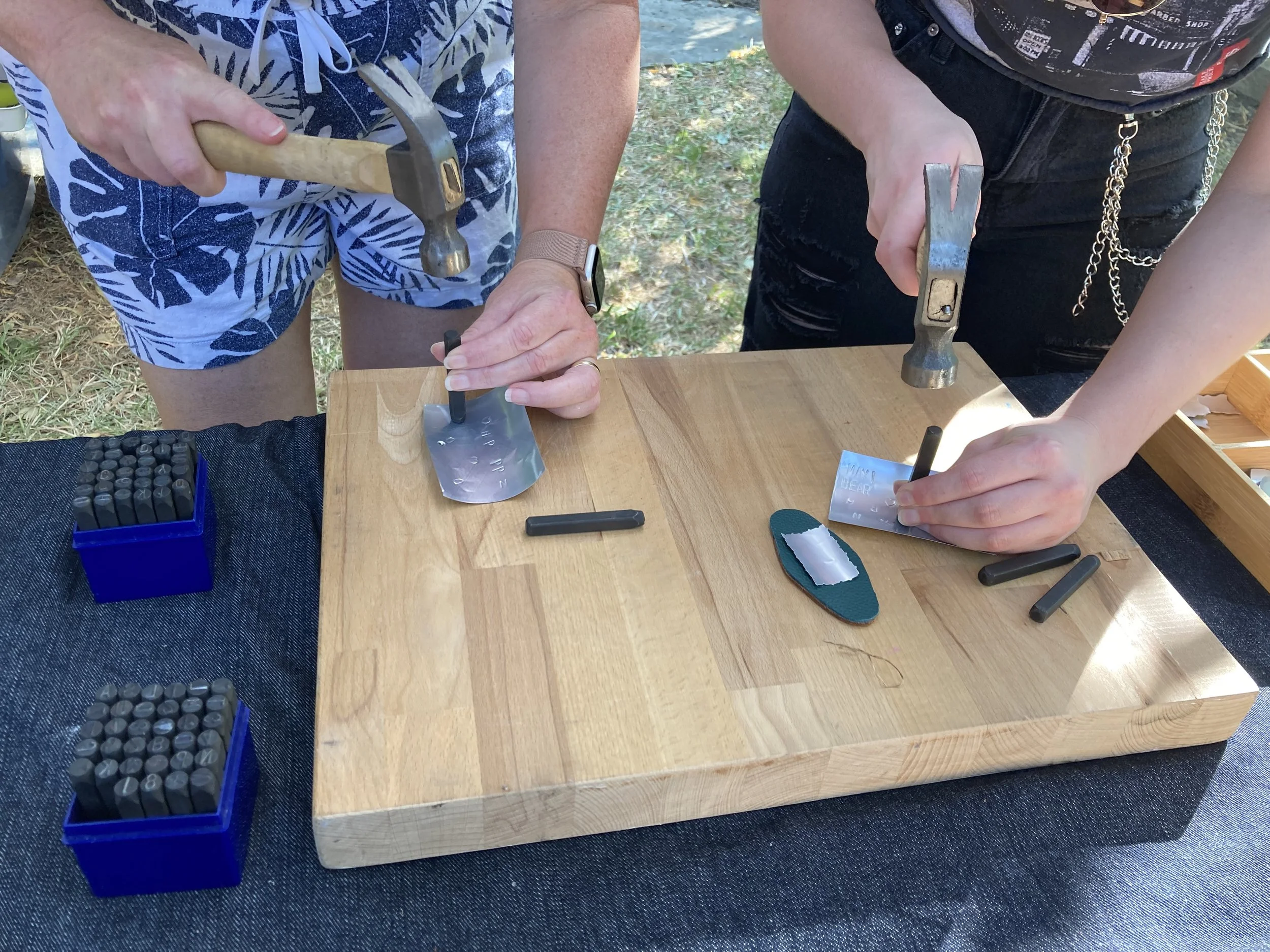 People using hammers to punch letters into recycled tin at a Kiki Knows Art workshop.