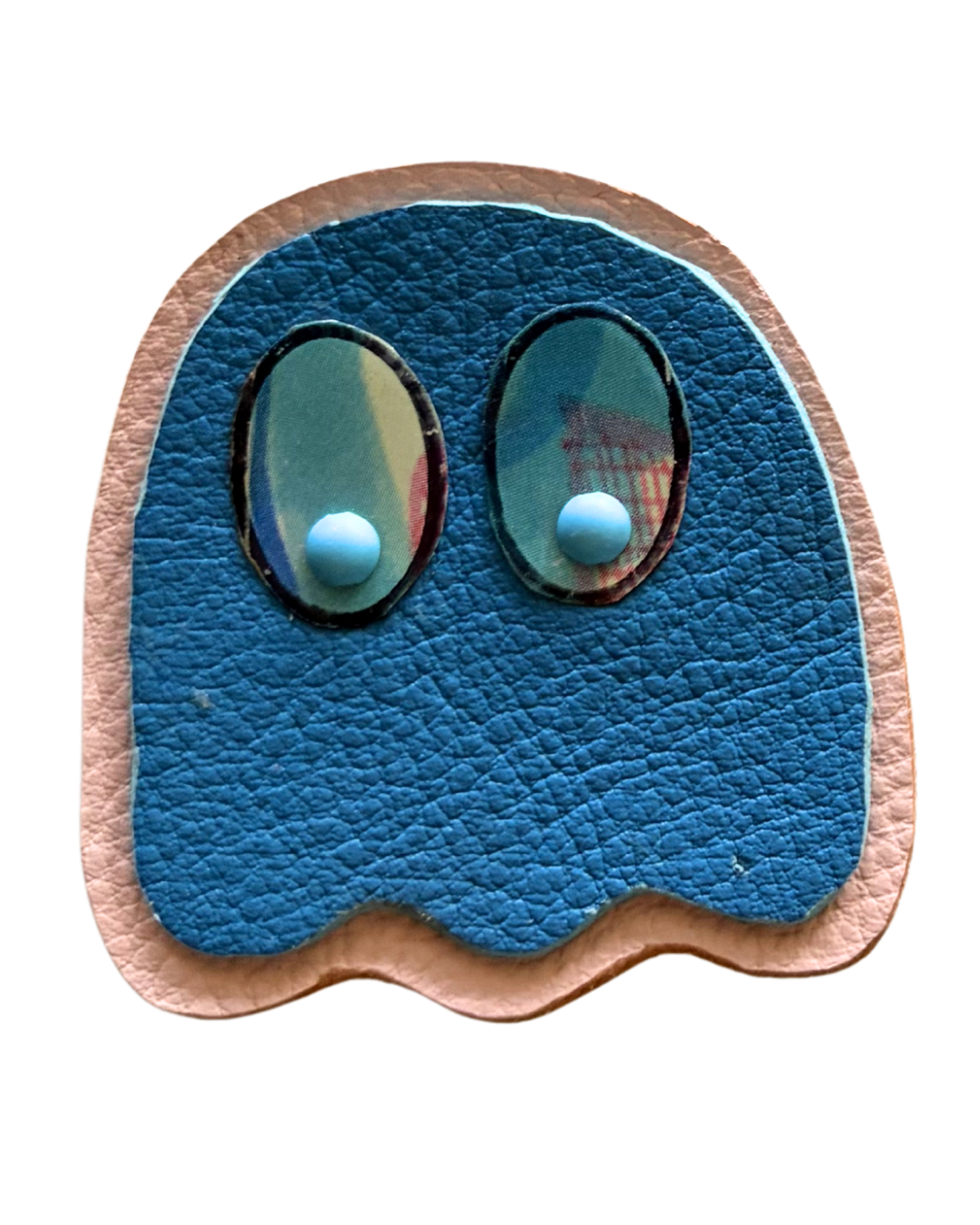 Close-up of a leather patch resembling a blue ghost from Pac-Man, with large oval eyes with reflective surfaces and pinkish skin around the edges.