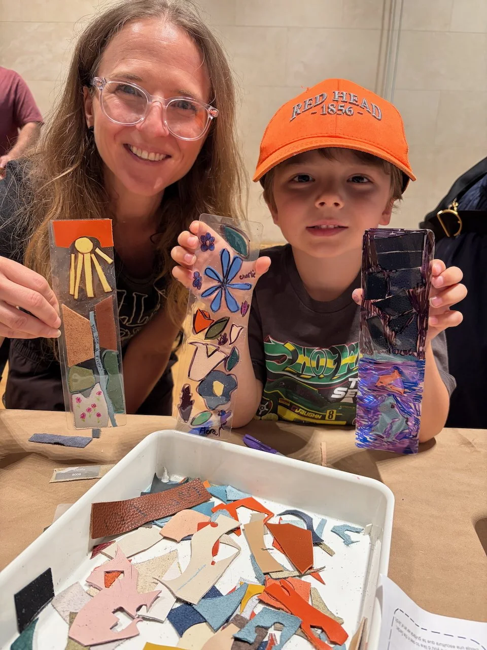A young woman and child show their handmade leather bookmarks at a Kiki Knows Art workshop.