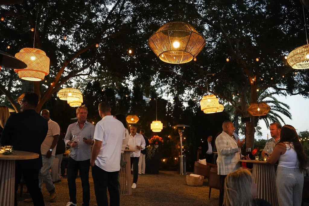People gathered at an outdoor evening Porsche event with string lights and paper lanterns hanging from trees.