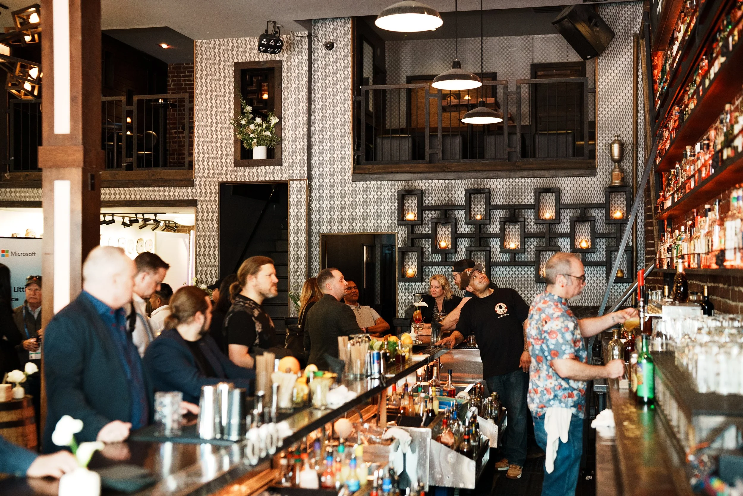 People gathering at a corporate Swig Microsoft event with shelves of alcohol bottles, modern lighting, and decorative wall elements.