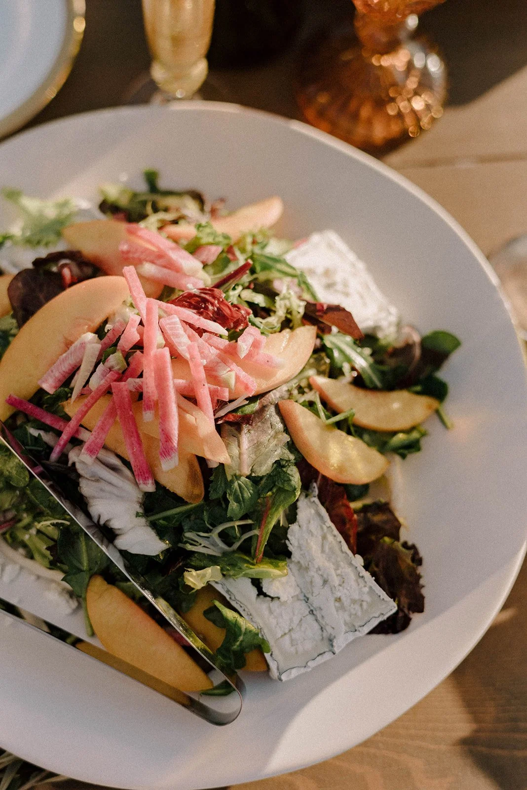 Mixed salad with greens, sliced apples, shredded radishes, and cheese on a white plate. A culinary menu designed by Urban Organics.