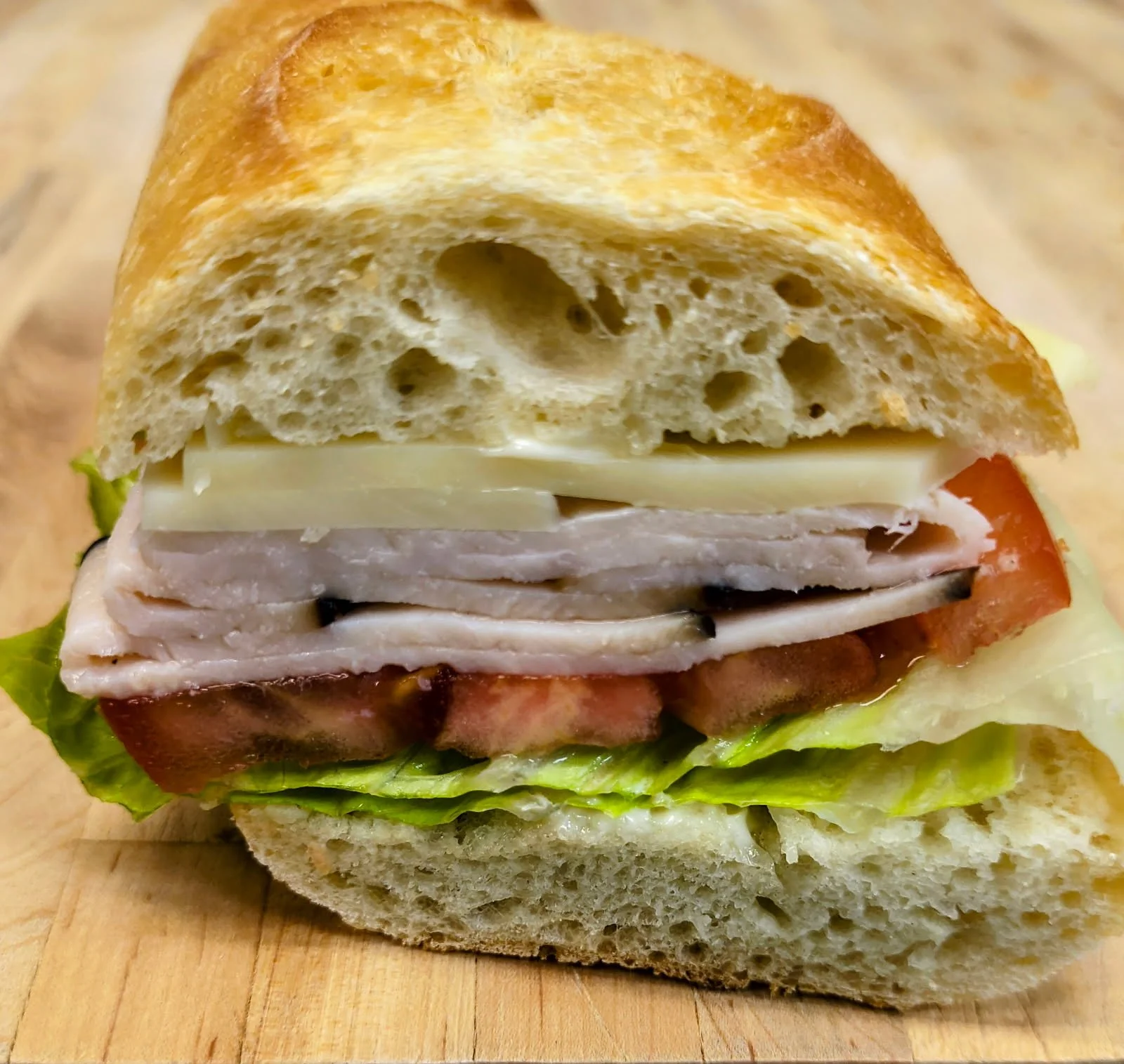 Close-up of a sandwich with turkey, cheese, tomato, lettuce, and bread on a wooden surface.