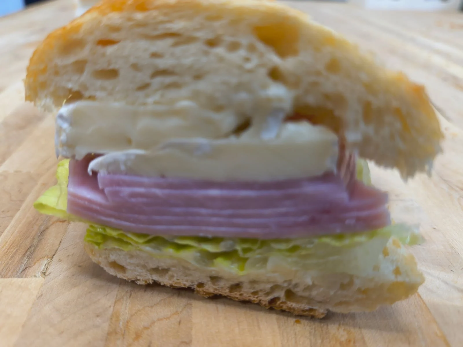Close-up of a sandwich with sliced ham, cheese, lettuce, and mayonnaise on a wooden cutting board.