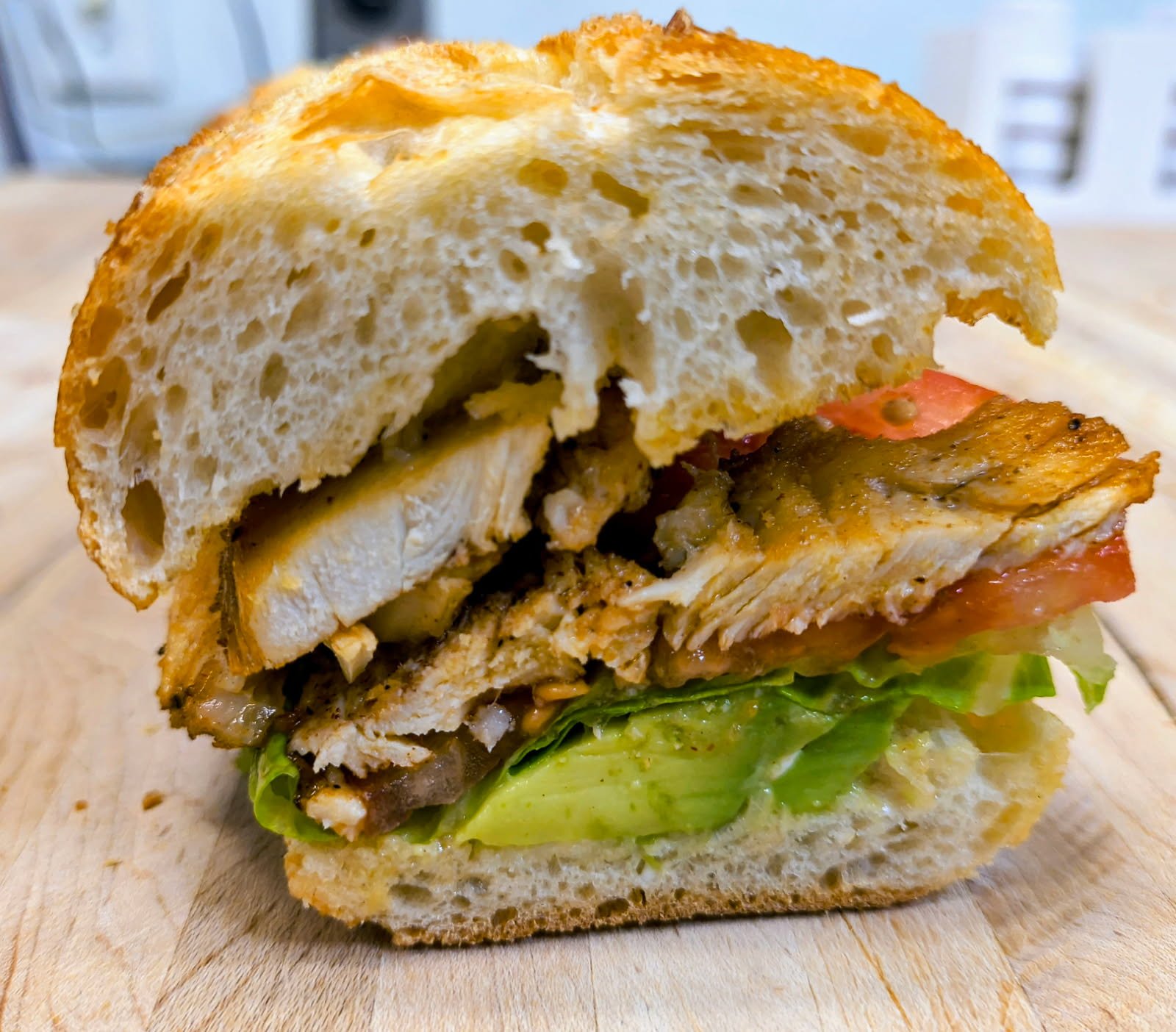 Cross-section of a sandwich with lettuce, tomato, grilled chicken, cheese, and bread.