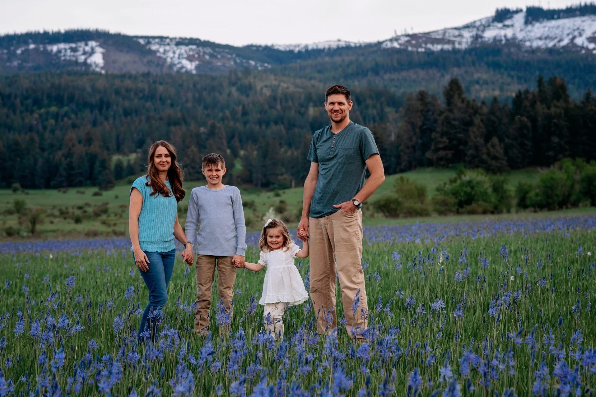 Family standing in from of snow-covered mountains, within a field of camas flowers taken near Grangeville Idaho.