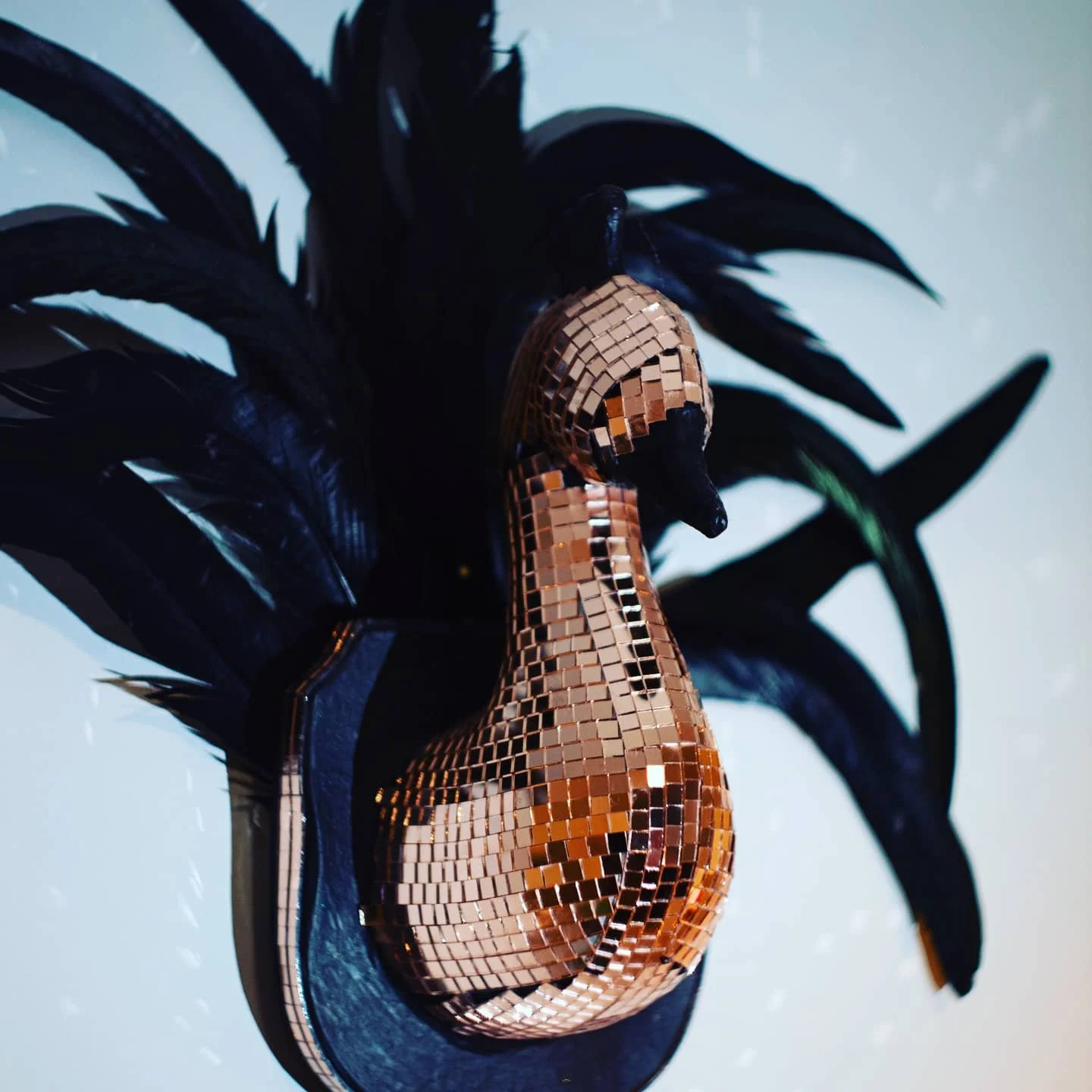 Decorative mirror sculpture of a woman with black leaves as hair, covered in small mirrored tiles, mounted on a black base.