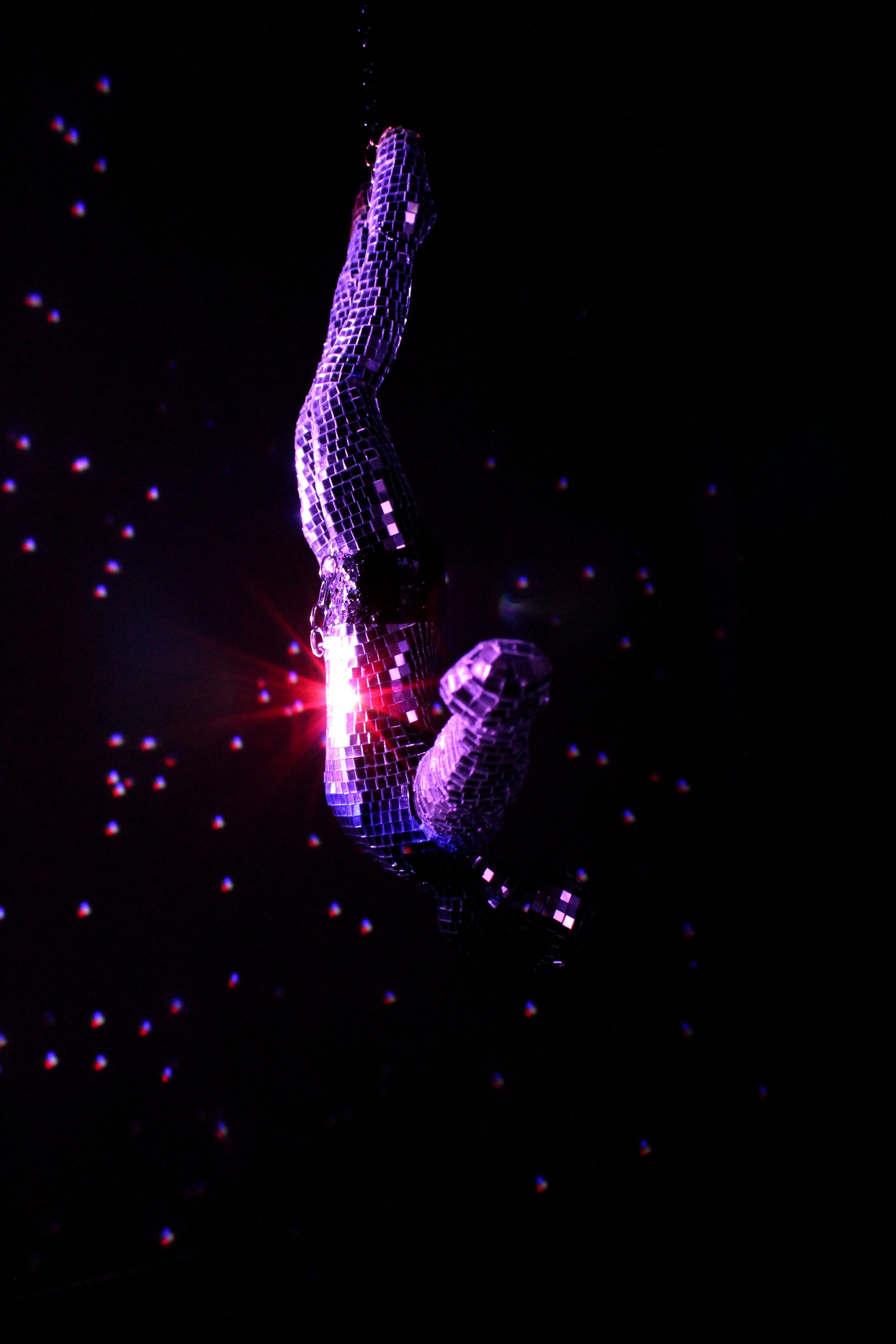 A bar of small square mirrors forming the shape of the letter 'J', illuminated by purple and pink lights against a black background, with red and blue light reflections.