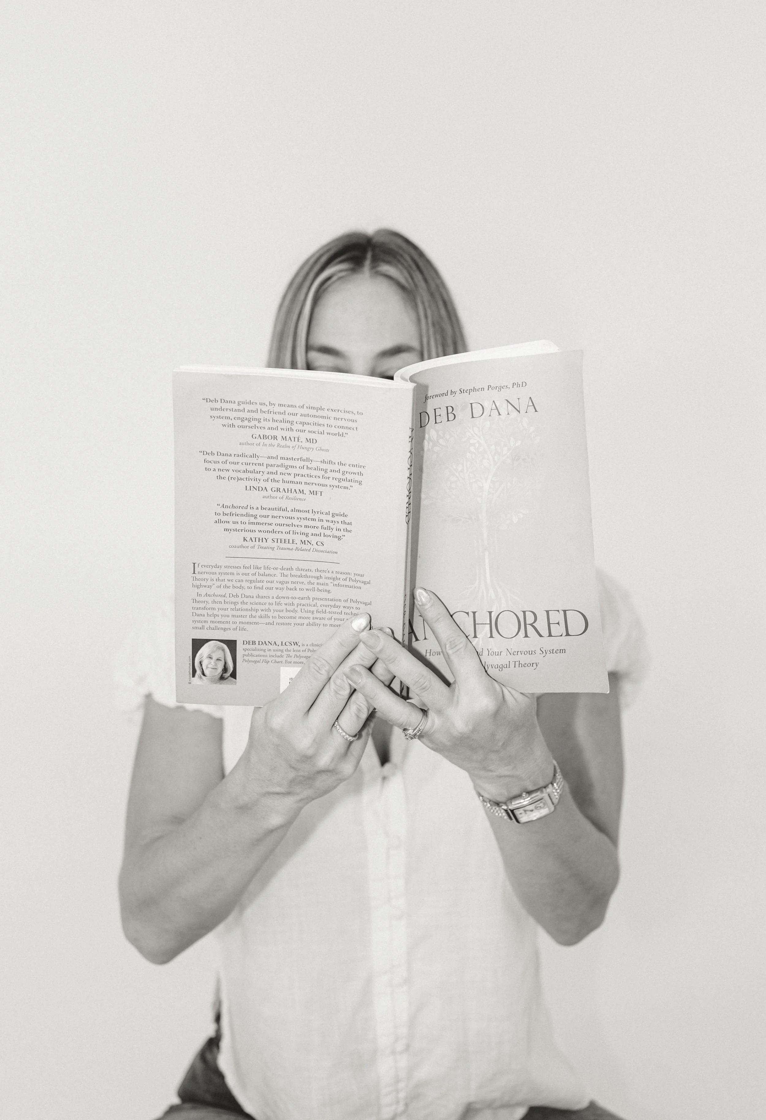 Person holding a book titled 'Anchored' by Deb Dana, with the person's face partially obscured by the book.