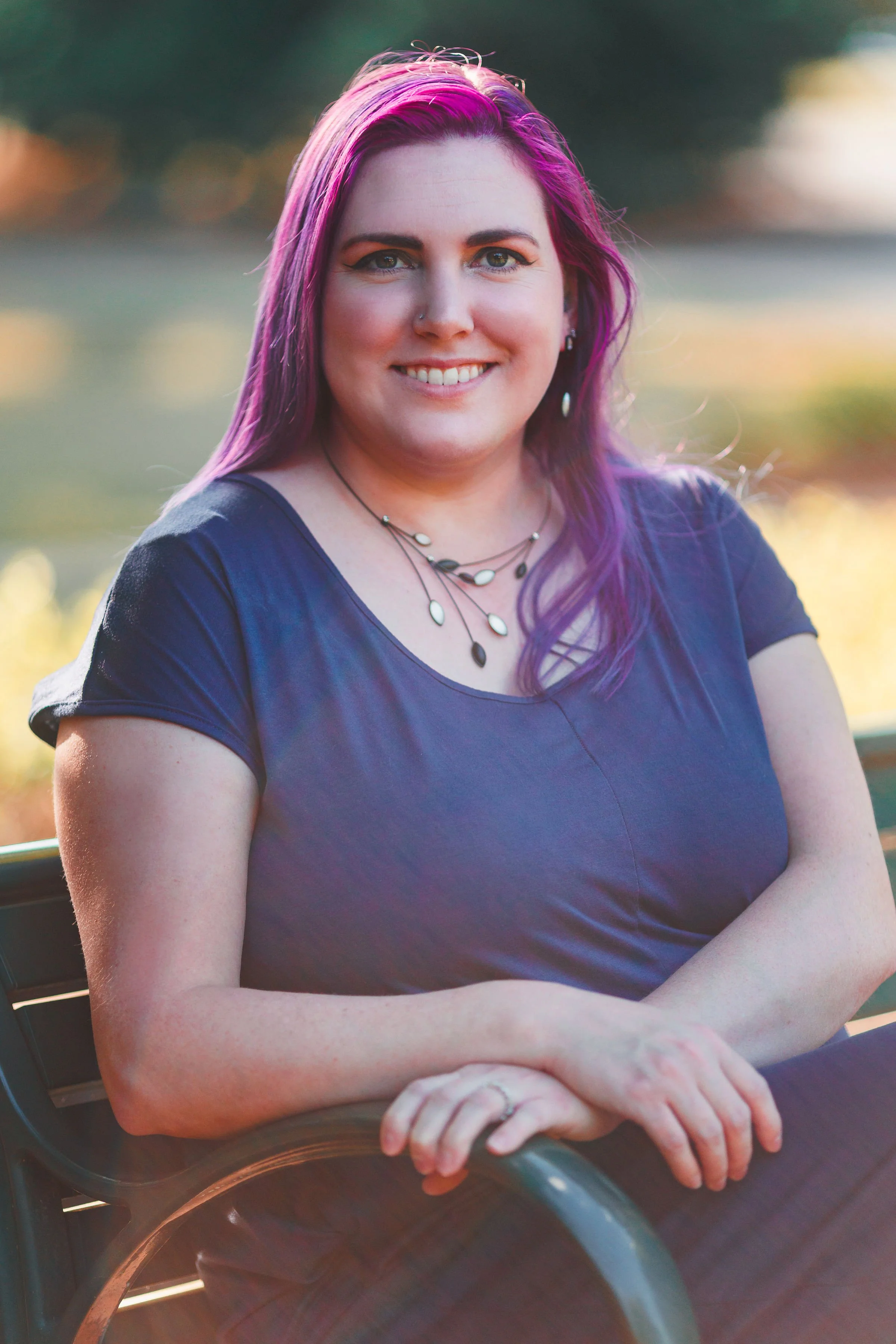 Brittany Porter, Principal Attorney at Law. A woman with bright pink and purple hair smiling outdoors, sitting with her arms crossed on a bench.