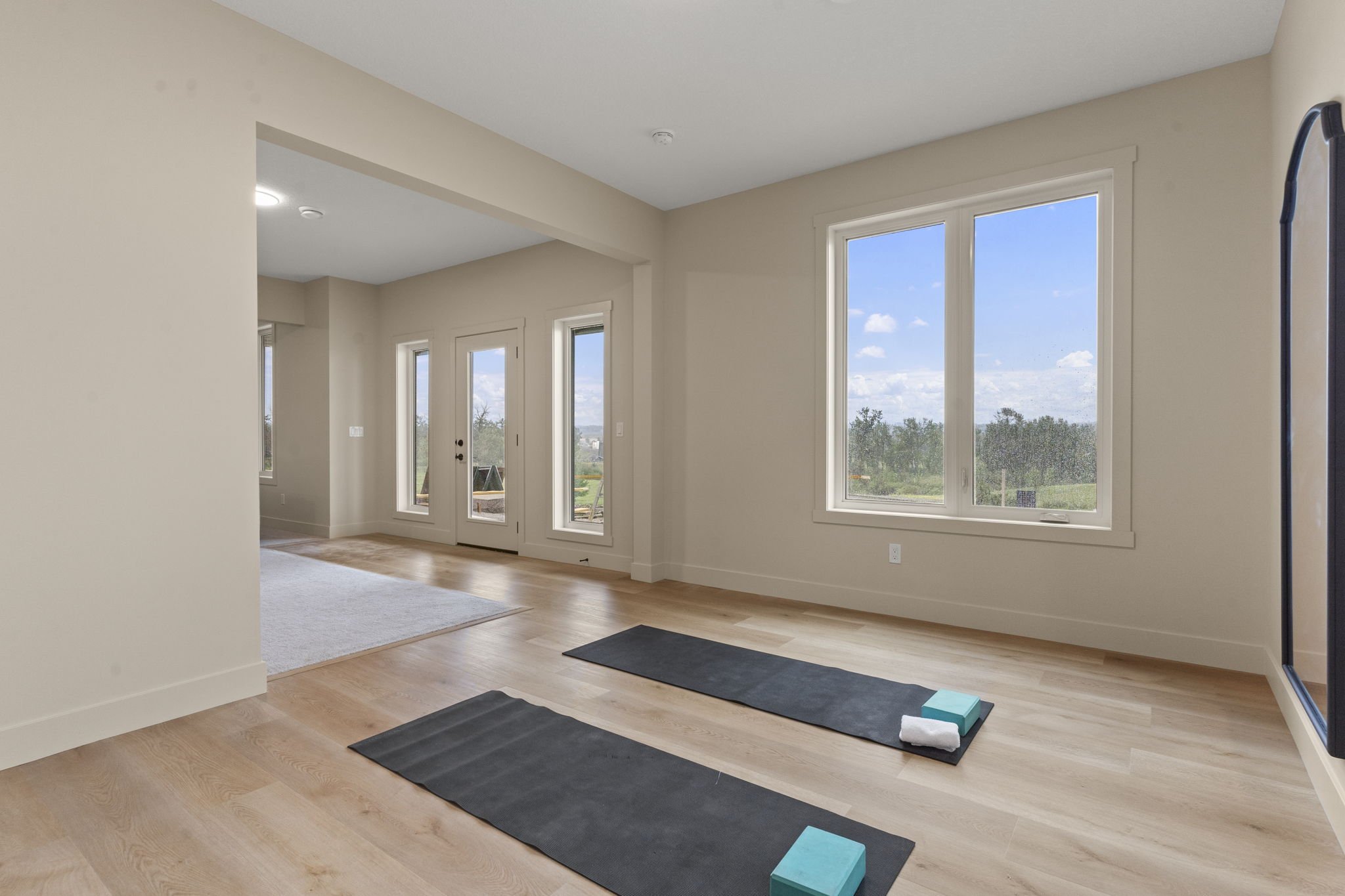 Unfinished living room with large windows overlooking a backyard, glass door, hardwood floors, and yoga mats with blocks and straps on the floor.