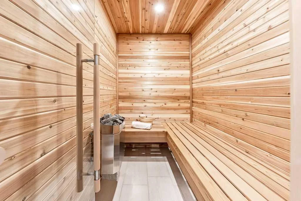 Interior of a wooden sauna with a bench, heat stones in a metal heater, a towel, and a water bucket.