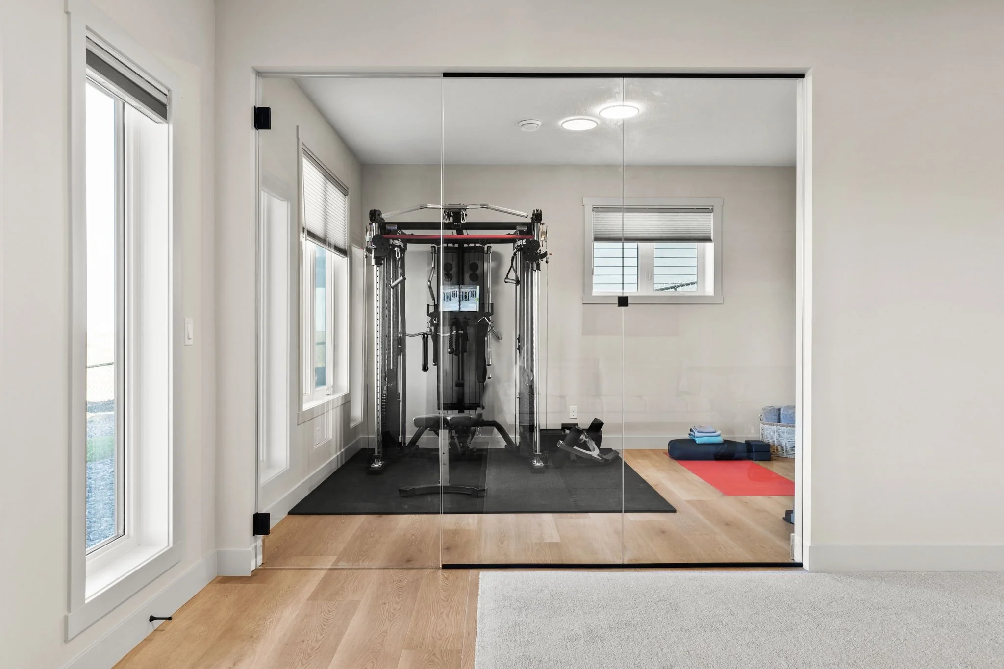 A home gym with a multi-function exercise machine inside a room with large windows, wooden floors, and a glass sliding door.