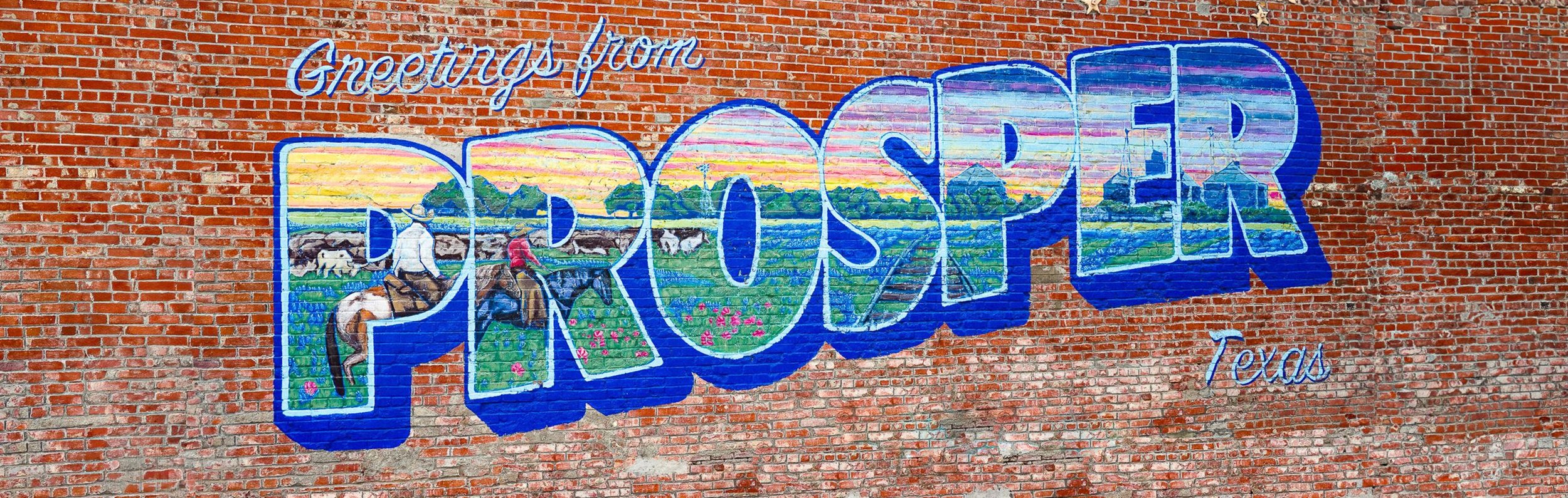 Colorful mural of the word 'Prouser' in large blue letters on a brick wall, with a rural scene inside the letters depicting farmers, fields, animals, and a sunset, and text 'Greetings from Texas' written above and below.