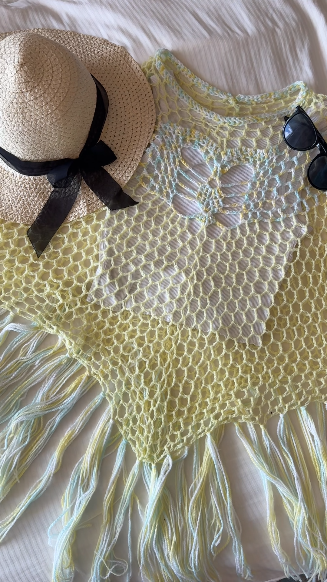 Pale yellow crochet Solace Poncho with a black bow, laid flat