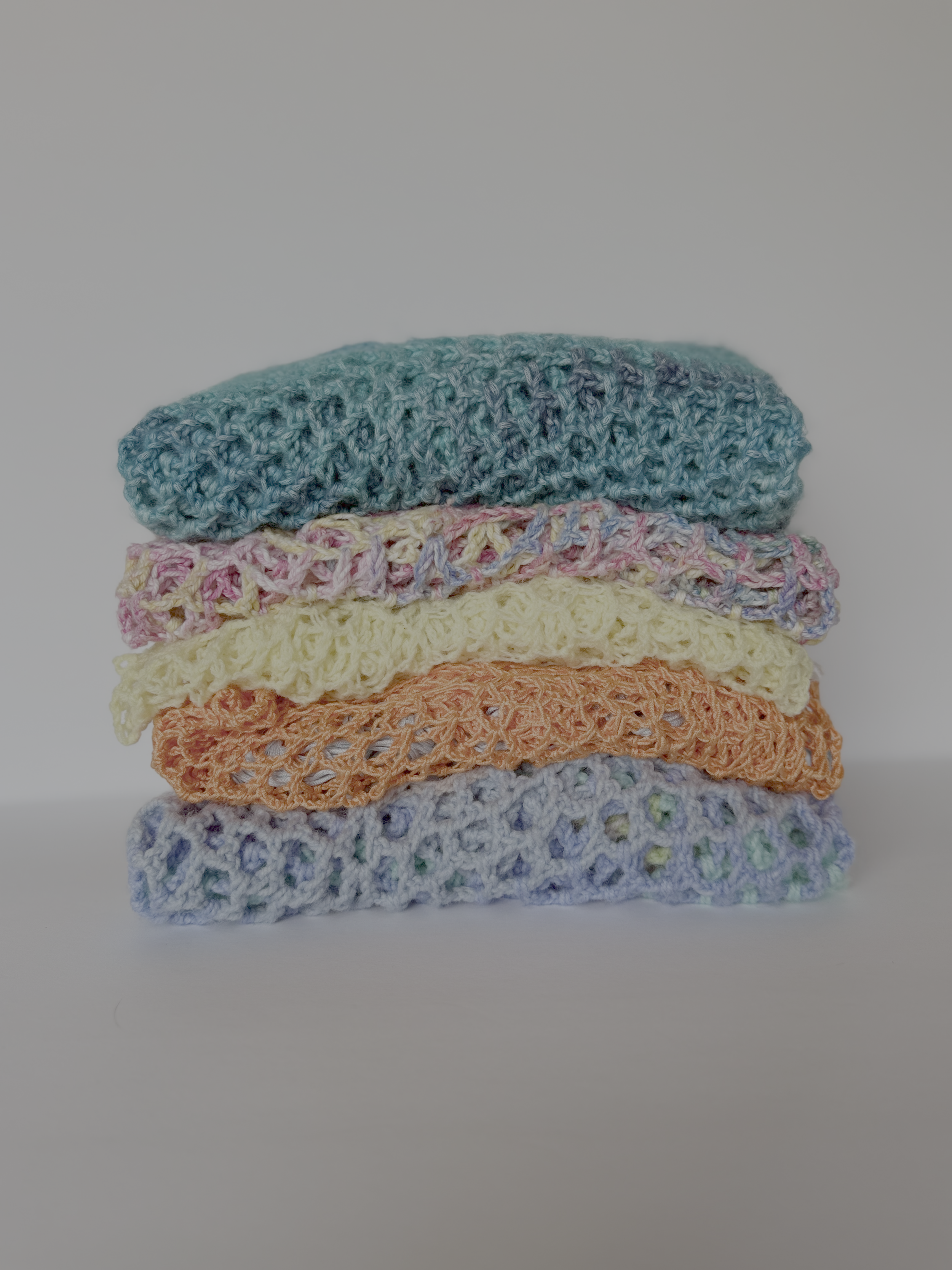 Folded stack of crochet Solace Ponchos in teal, yellow, orange and pastel multi