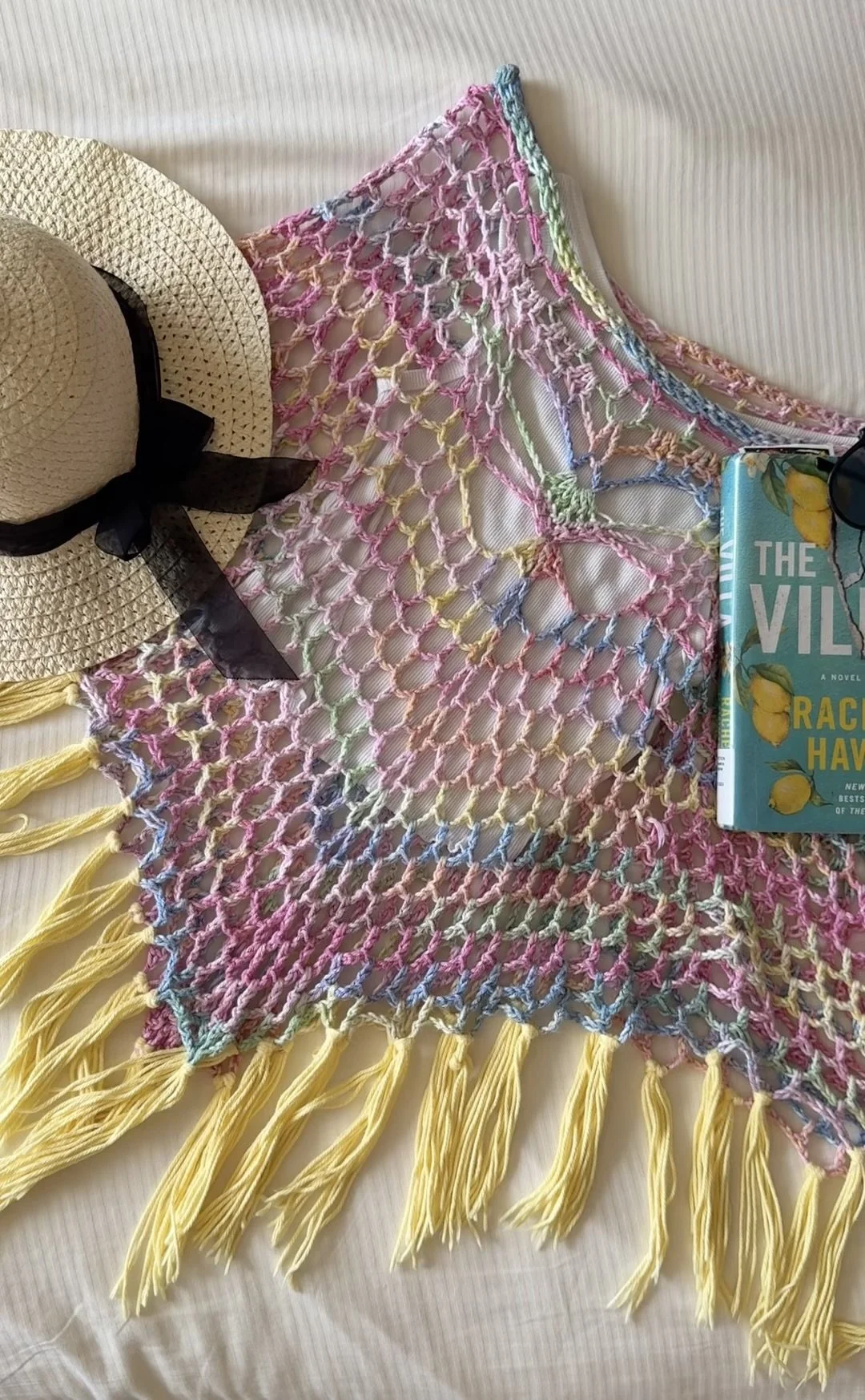 Pastel rainbow crochet poncho with butterfly motif, laid flat with a straw hat and a book
