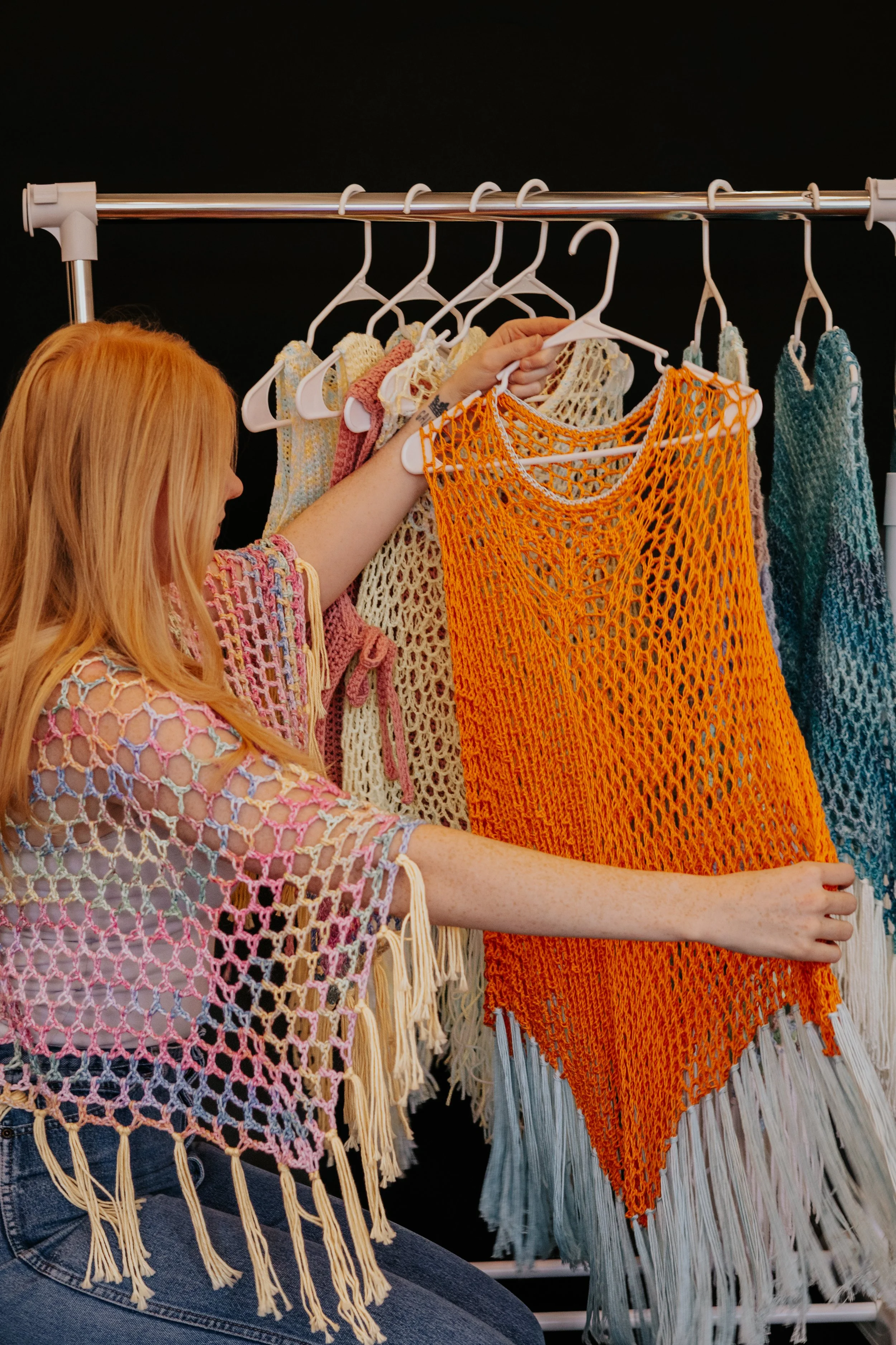 Orange and yellow handmade crochet pieces on a garment rack