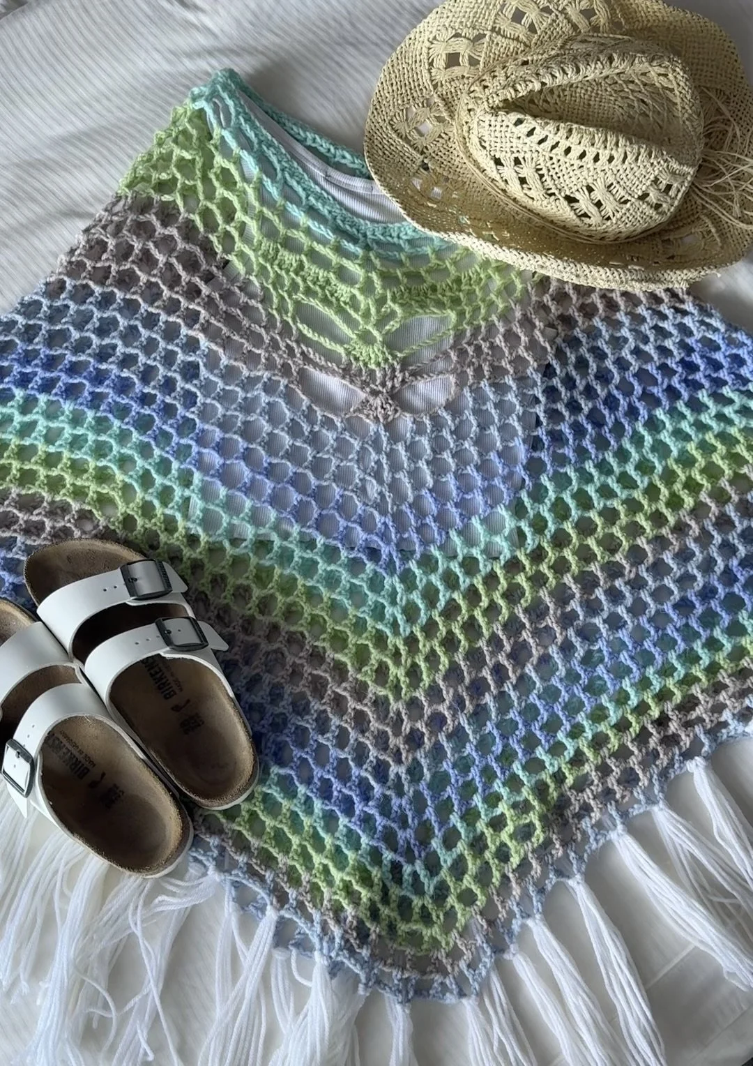 Pastel multi crochet Solace Poncho laid flat with sandals and a sun hat