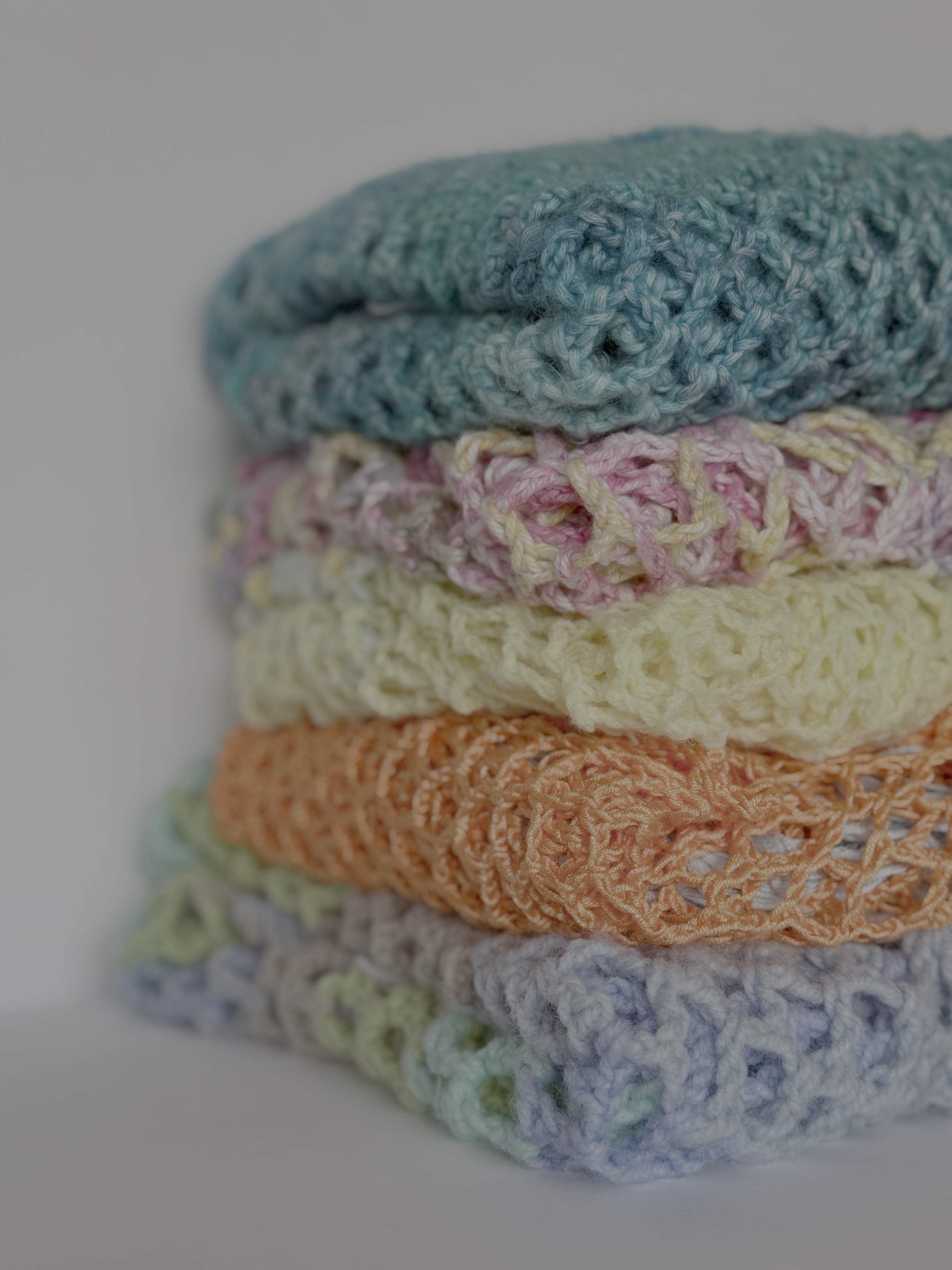Close-up of folded crochet Solace Ponchos showing the open stitch in teal, yellow and orange