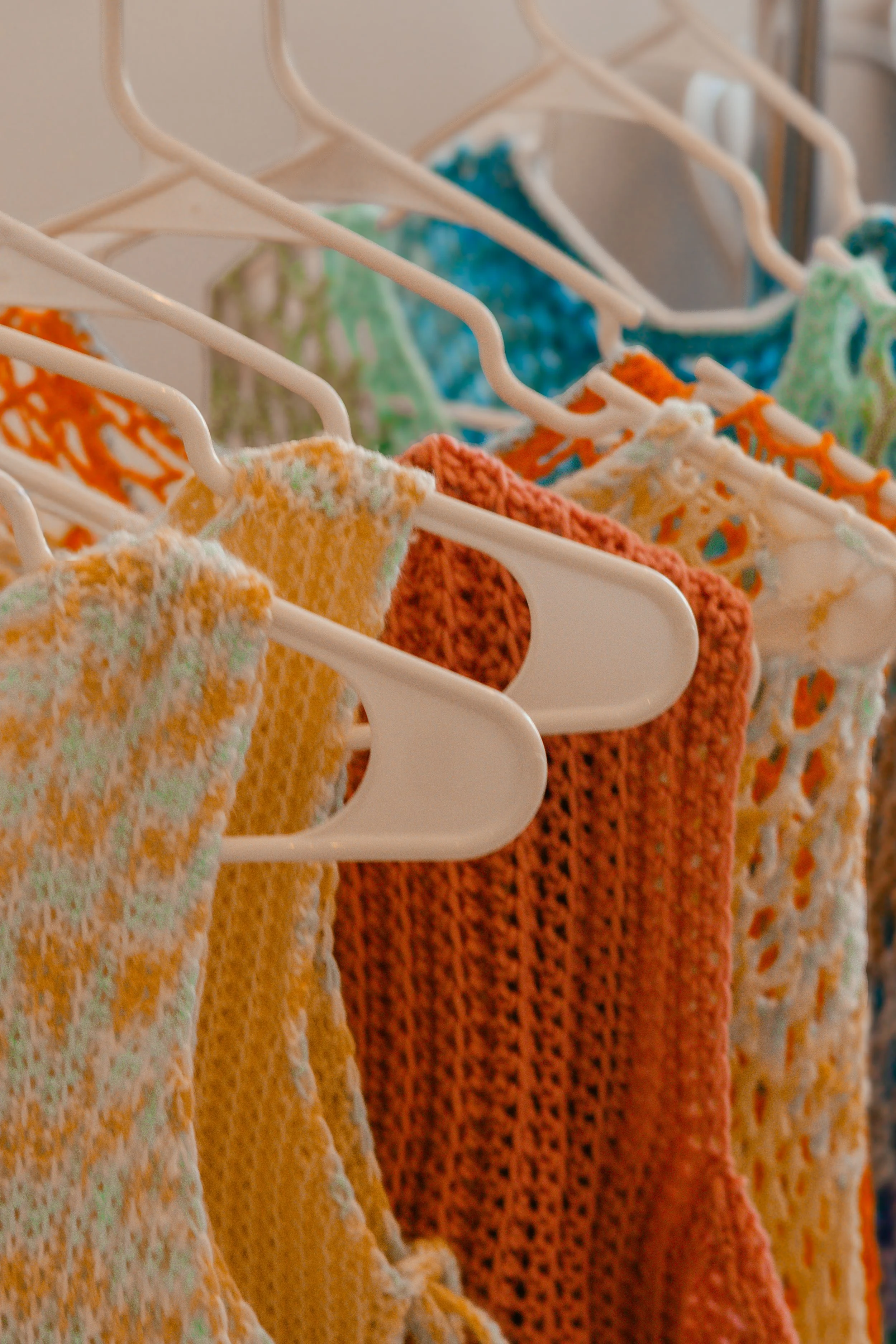 Handmade crochet ponchos in orange, yellow and teal on hangers