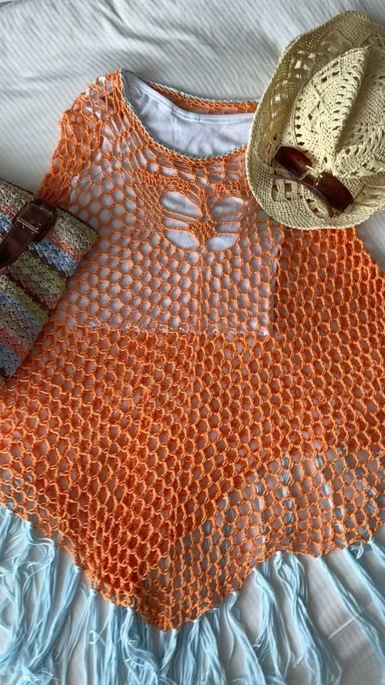 Orange bamboo crochet Solace Poncho with butterfly motif, laid flat with a sun hat