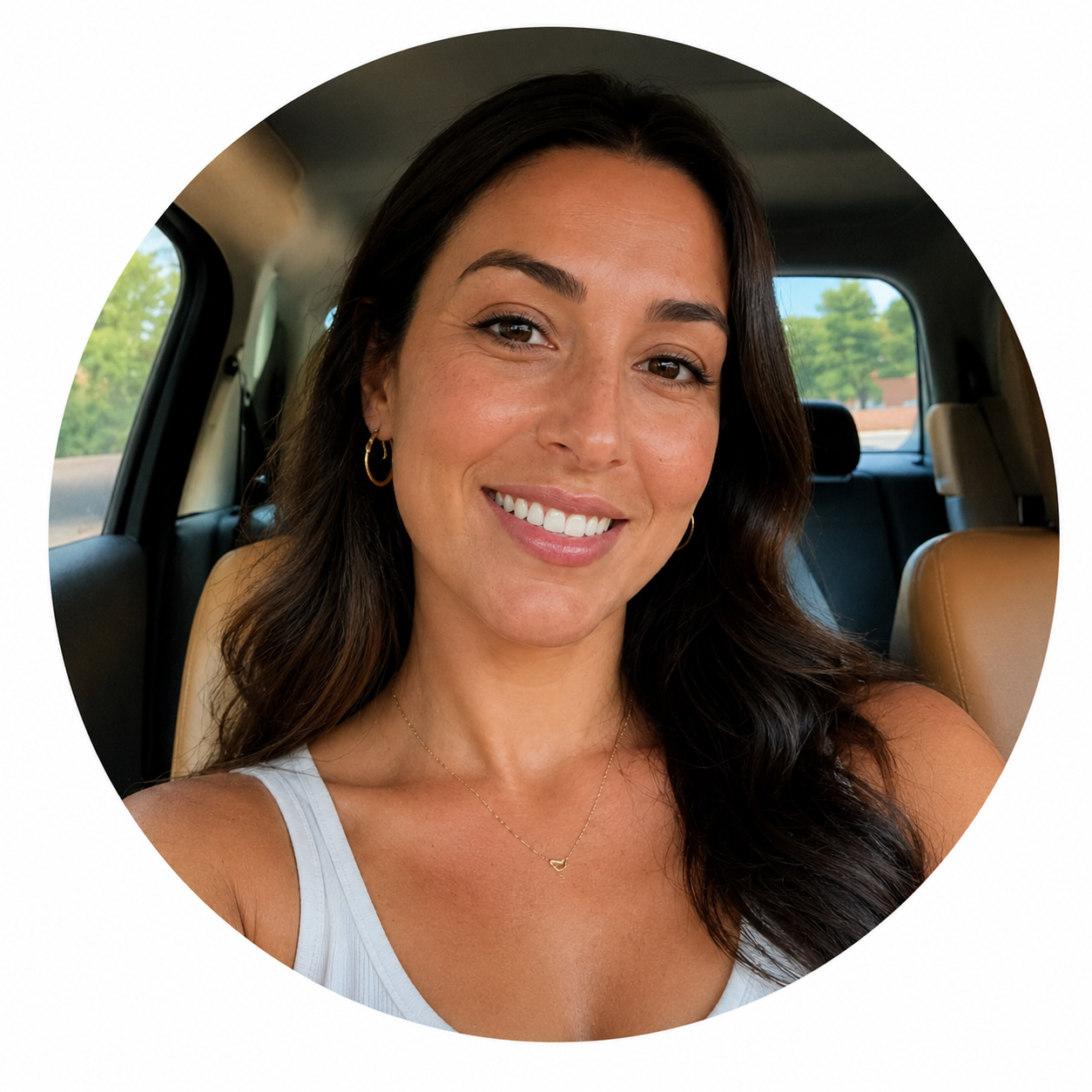Close-up of a smiling woman with dark hair, wearing hoop earrings and a white tank top, sitting in a car.
