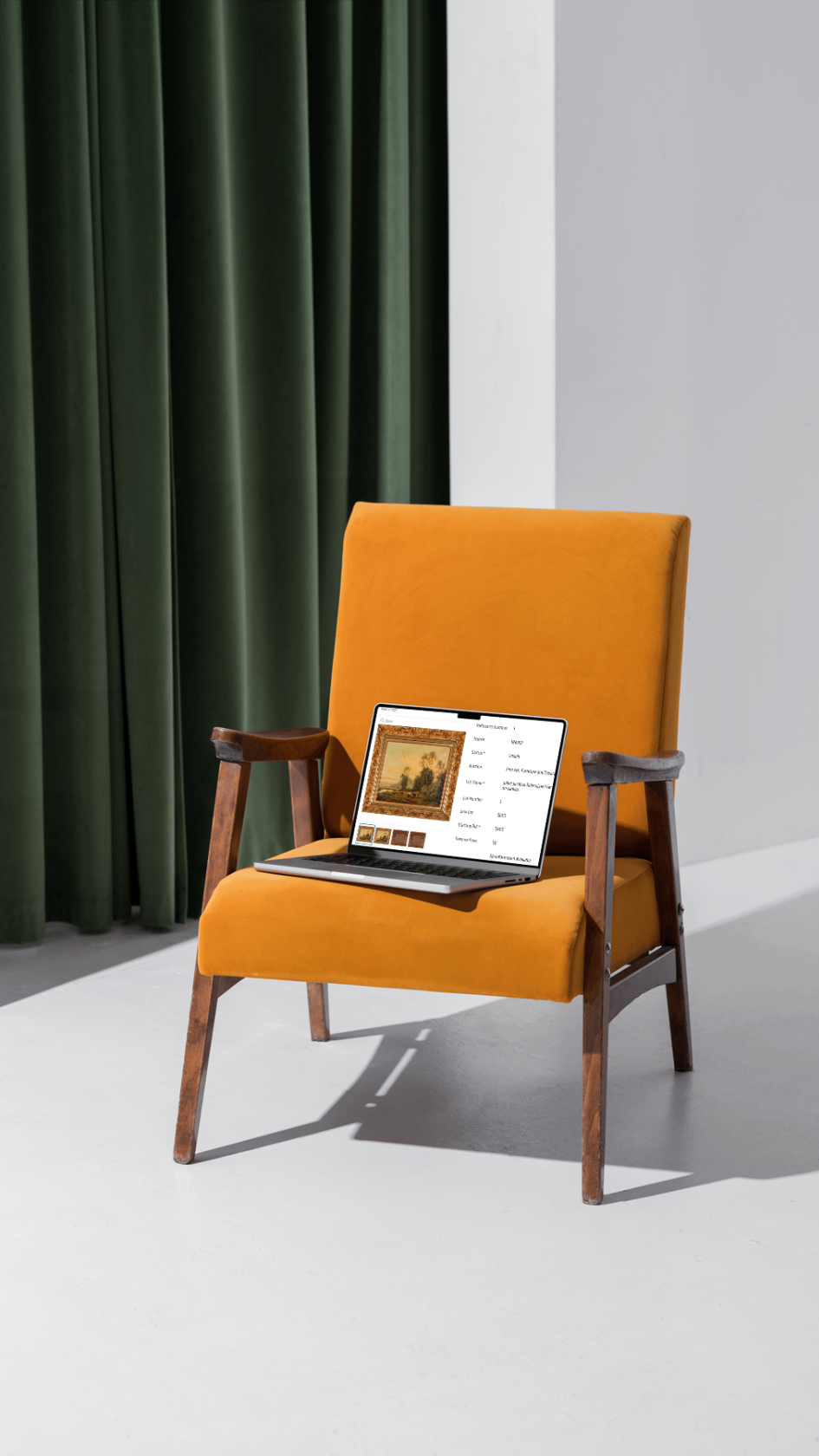 Open laptop displaying artwork on a mustard-yellow vintage armchair beside dark green curtains