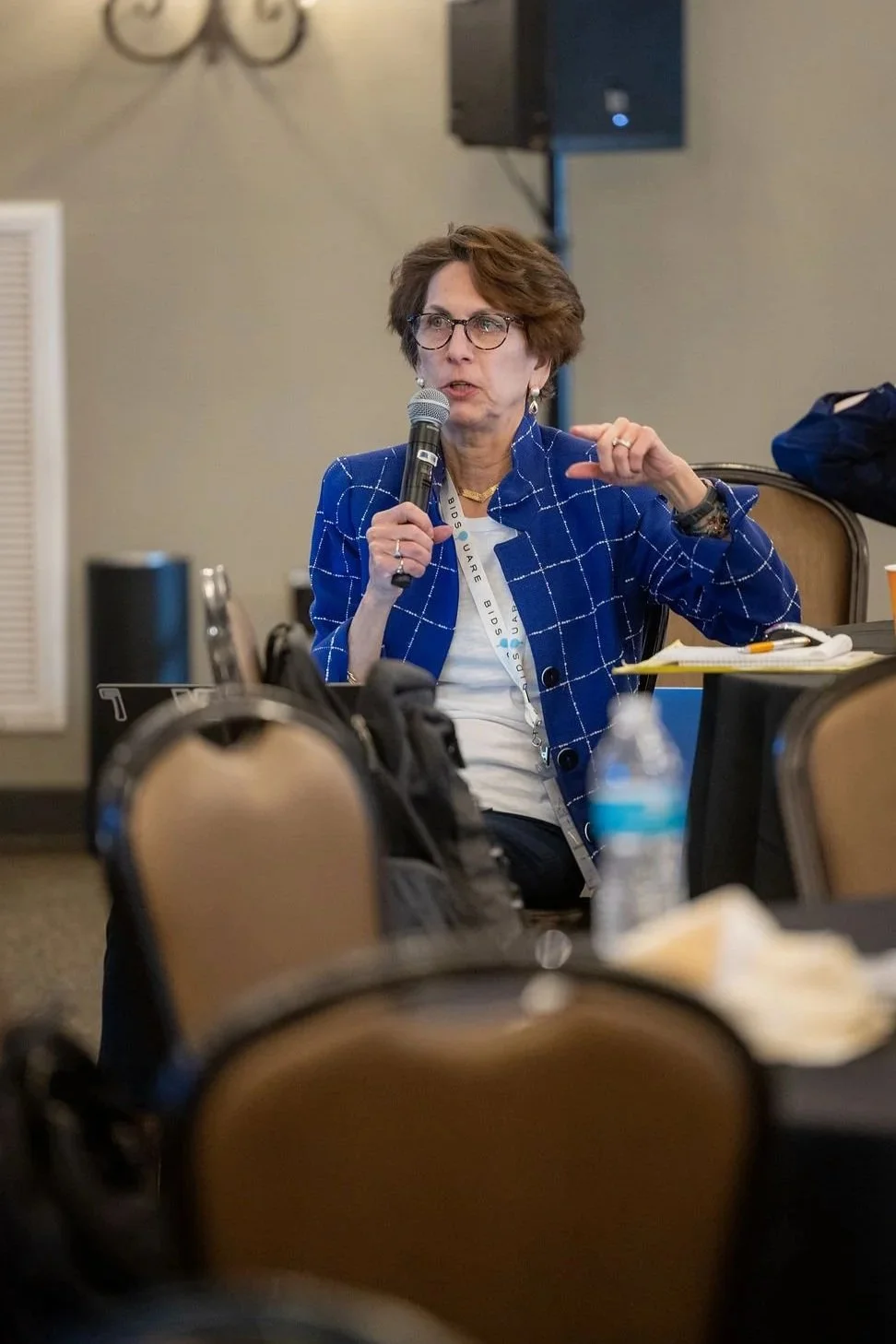 Woman in glasses speaking into a microphone during a meeting