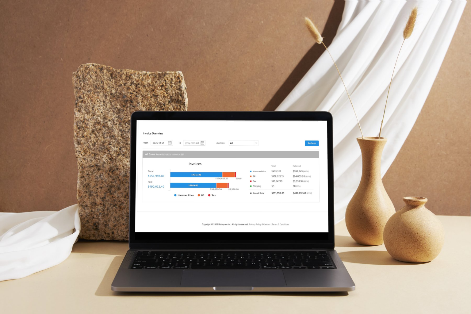 Laptop displaying an invoice overview dashboard with payment totals and bar charts on a styled desk beside ceramic vases.