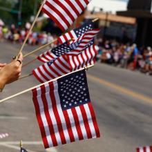 Multiple American flags being held by a person during a parade, with spectators watching along the street.