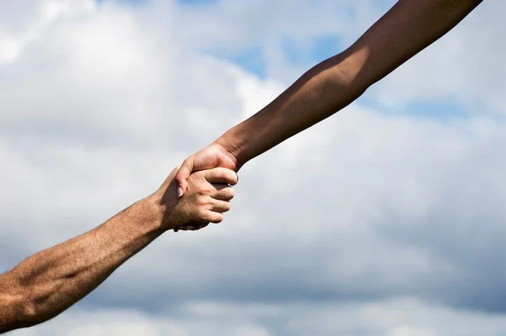 Two hands, one with darker skin, holding each other against a cloudy sky background.