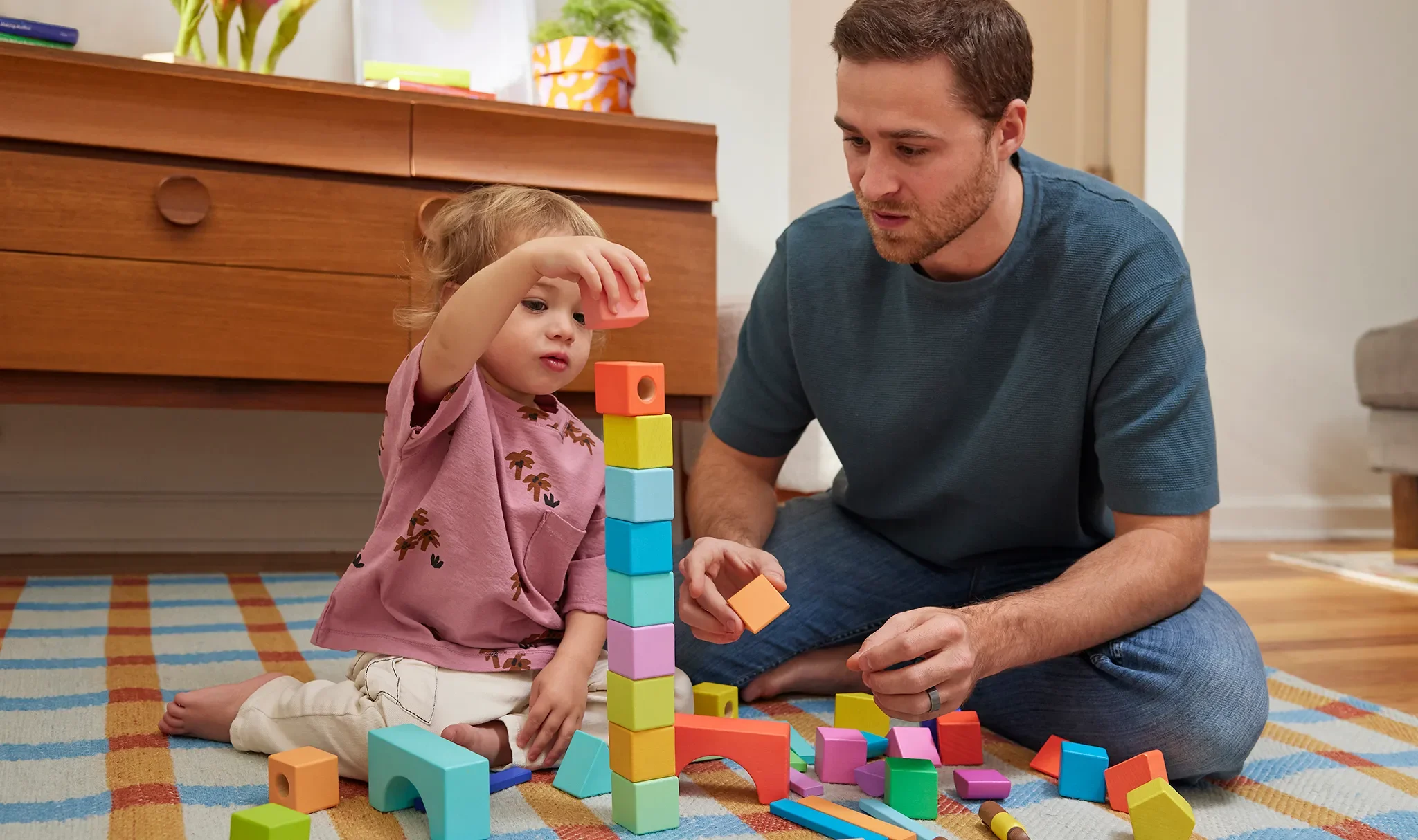 A young girl and a man playing with colorful building blocks on a rug in a living room.