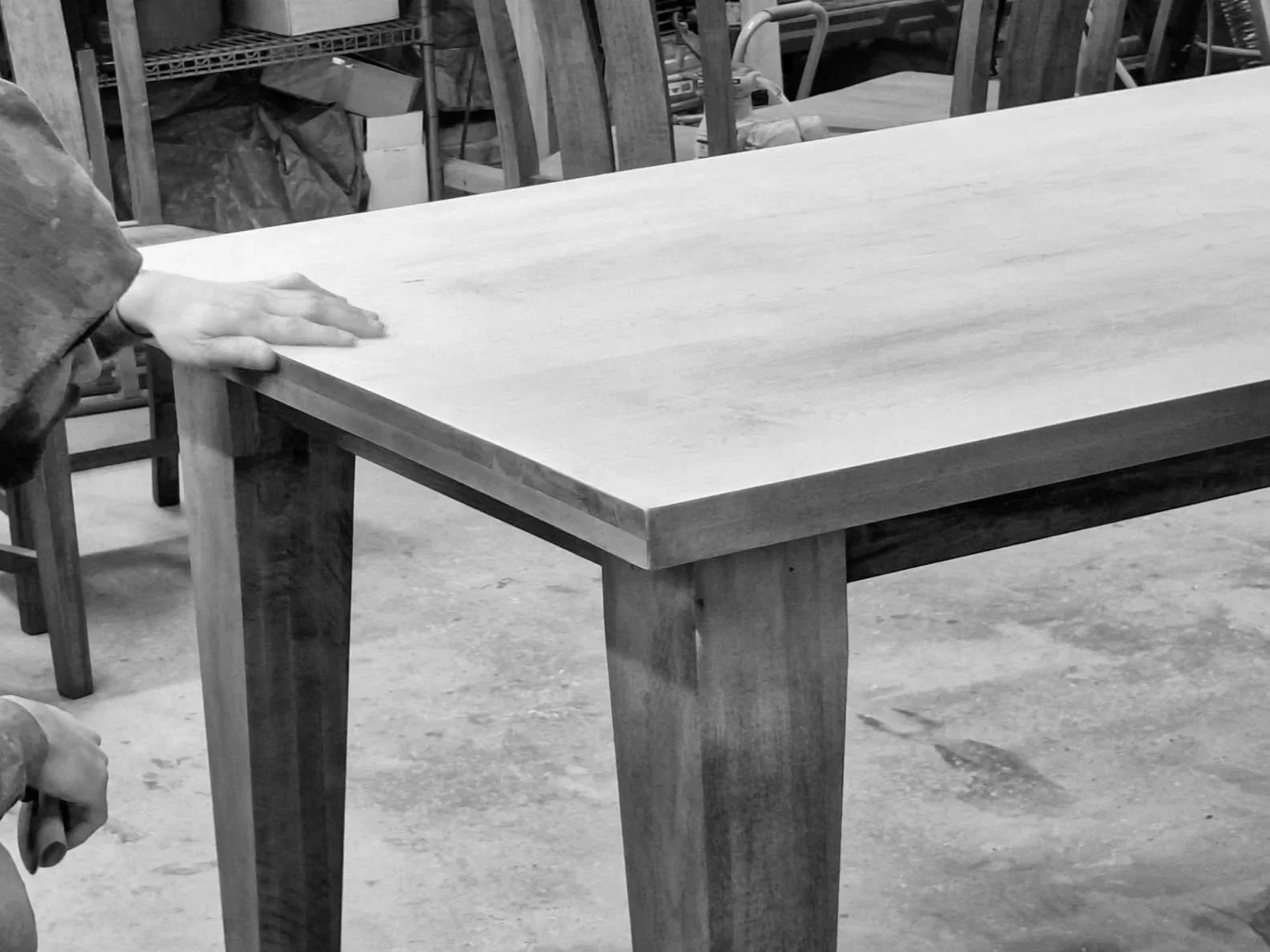Person inspecting or measuring the top of a wooden table in a woodworking or carpentry shop.