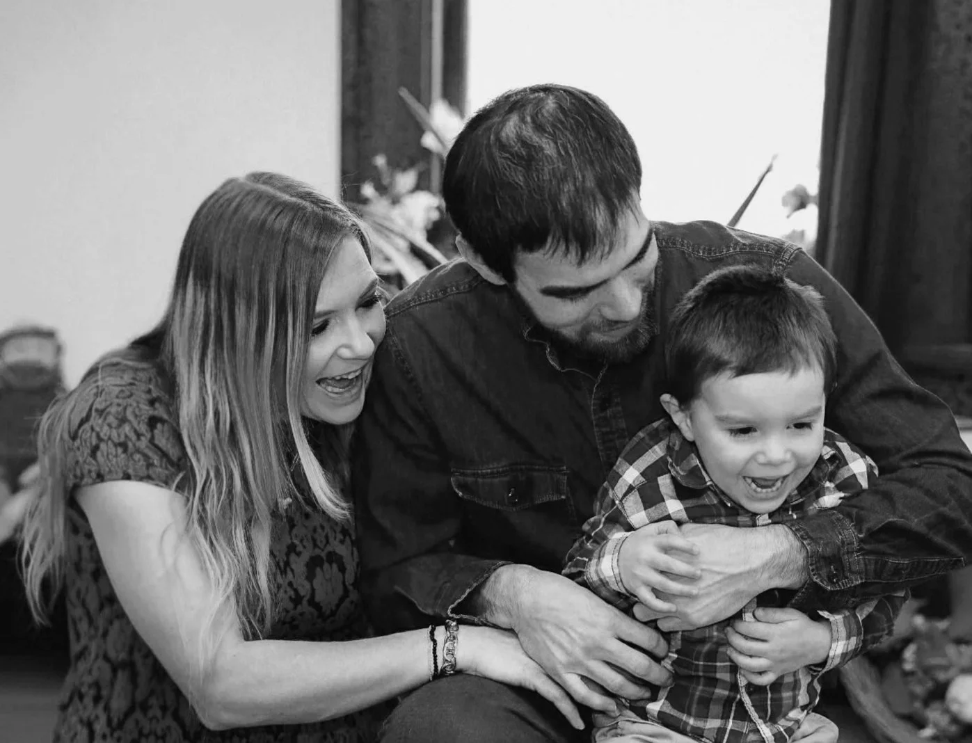 A happy family playing together indoors, with a woman, a man, and a young boy.