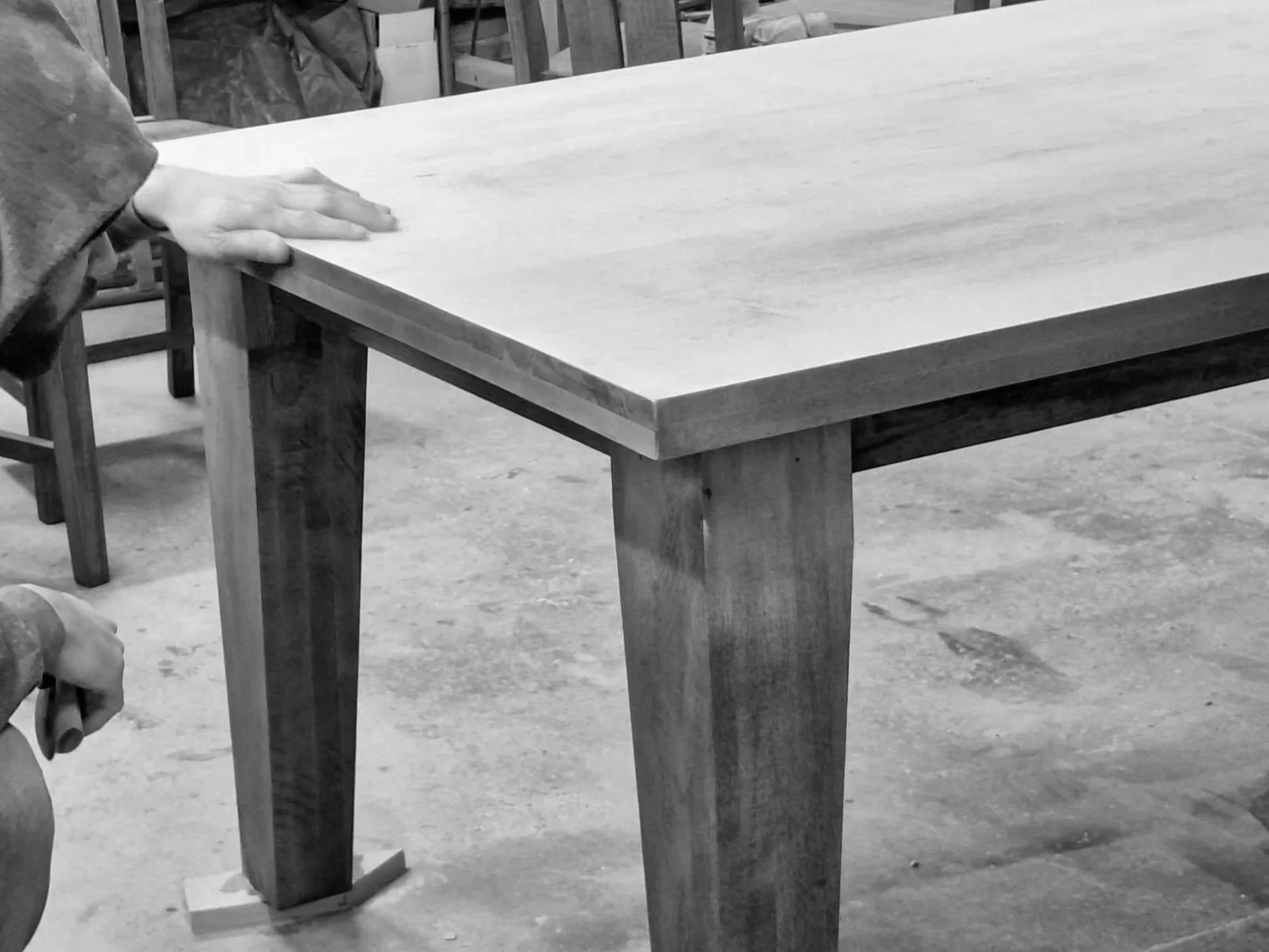A person is holding a tool and working on a wooden table in a workshop setting.