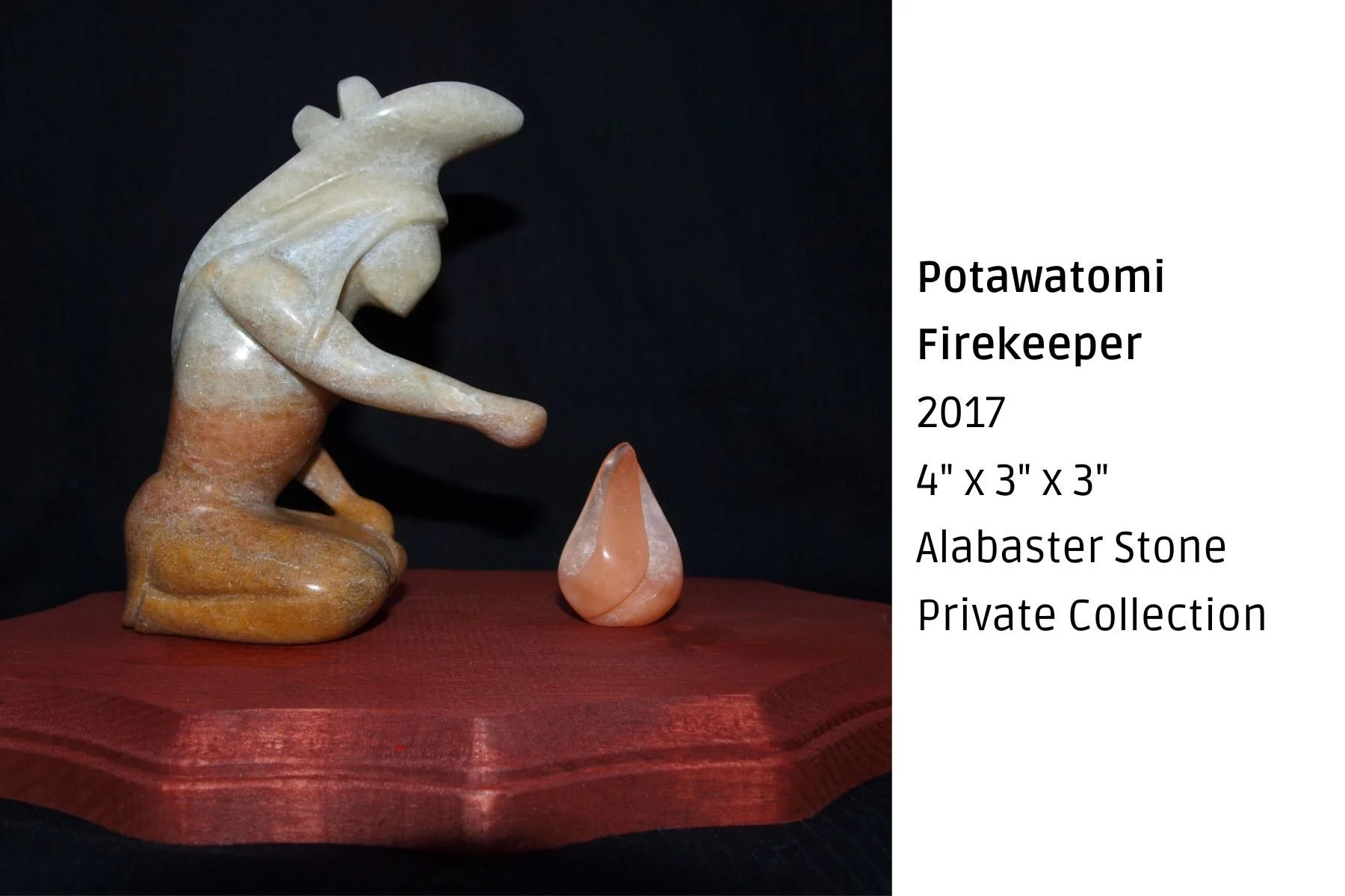 A carved alabaster stone figure of a firekeeper in a kneeling pose with a downward gaze, placed on a wooden platform. Next to the figure is a small, teardrop-shaped piece of pinkish alabaster stone. The background is black, emphasizing the sculpture 