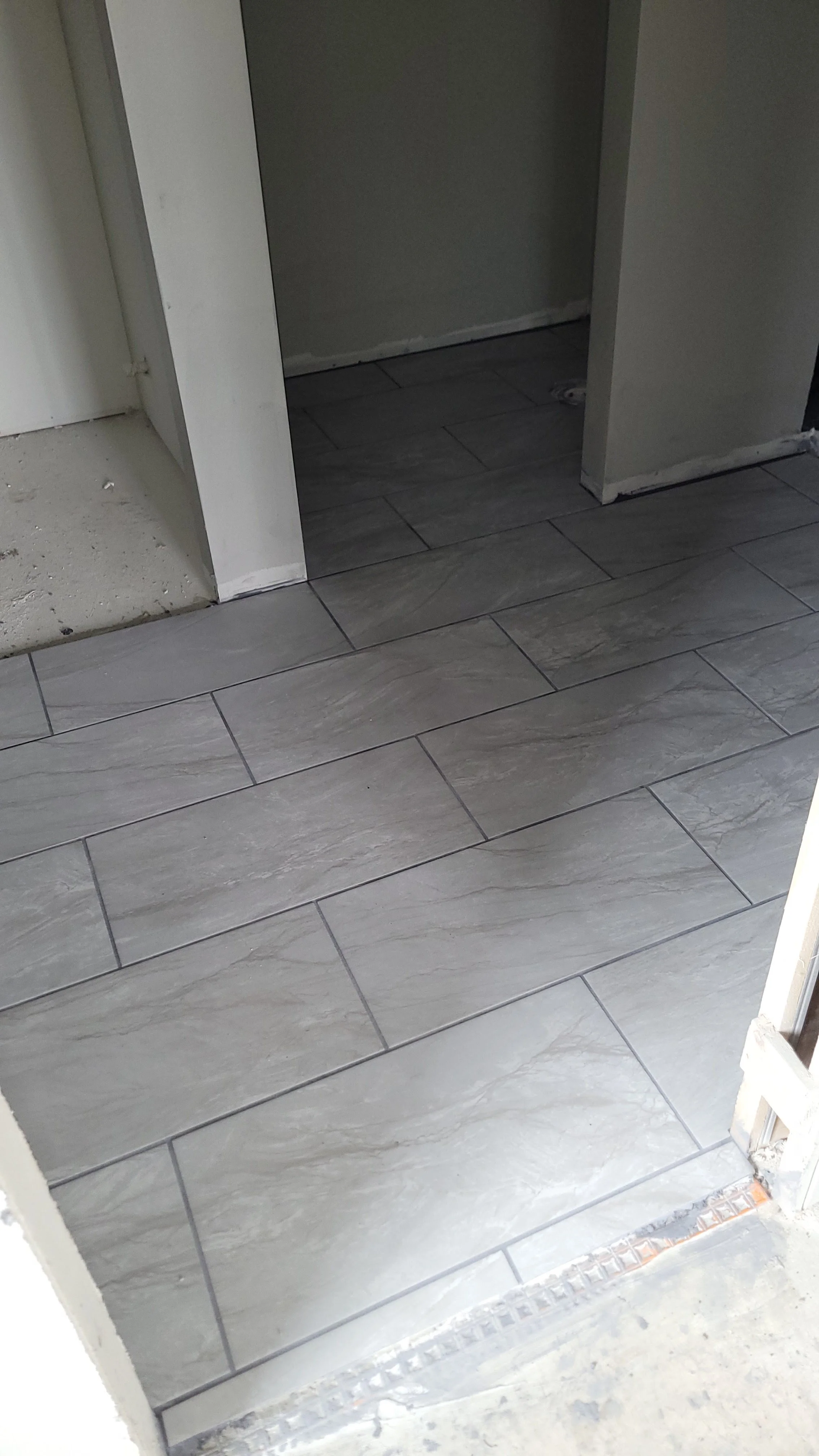 Interior space with new gray tiles on the floor and unfinished doorway with visible drywall and construction materials.