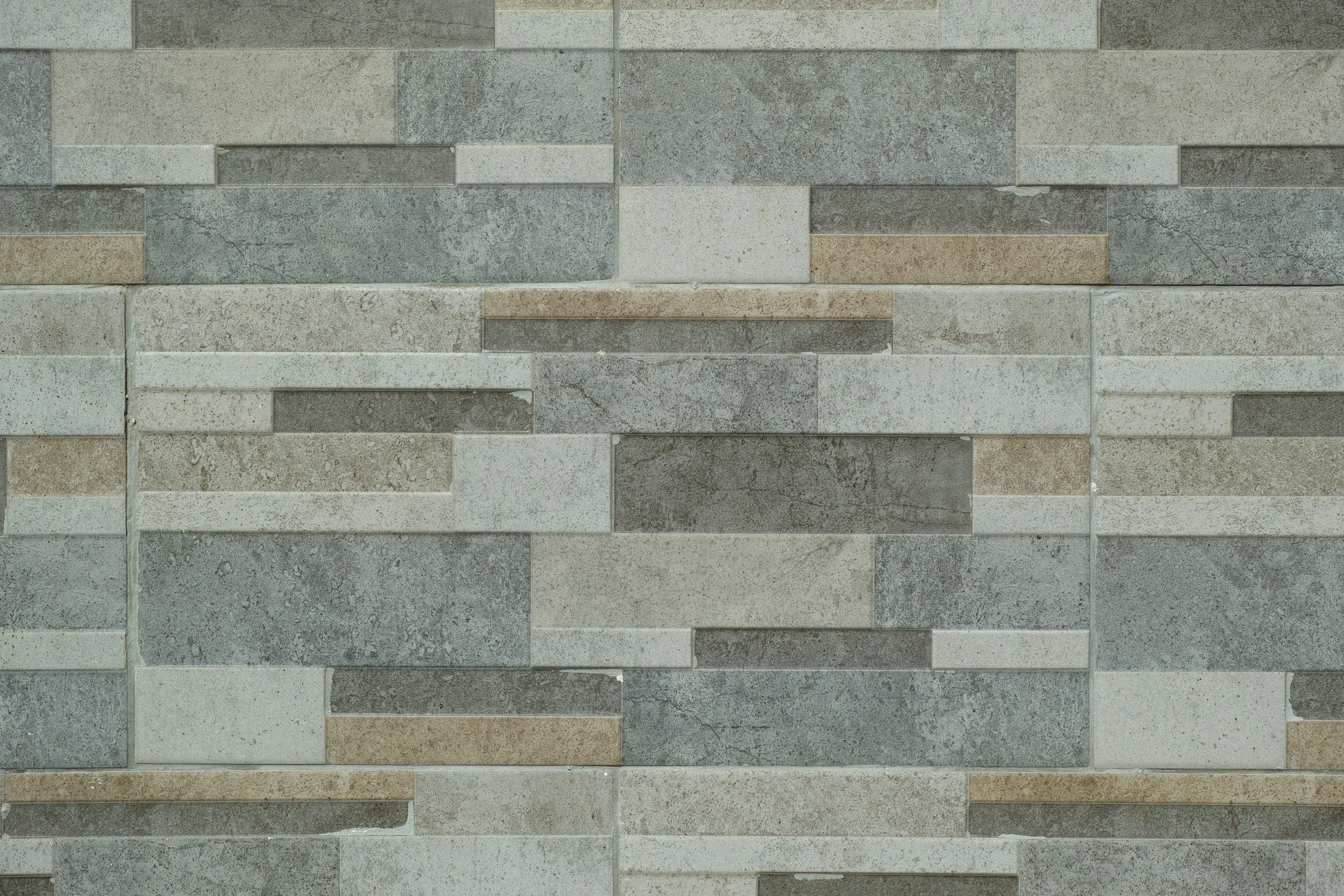 A mosaic wall made of small rectangular stone tiles in shades of gray, beige, and light brown arranged in a horizontal pattern.