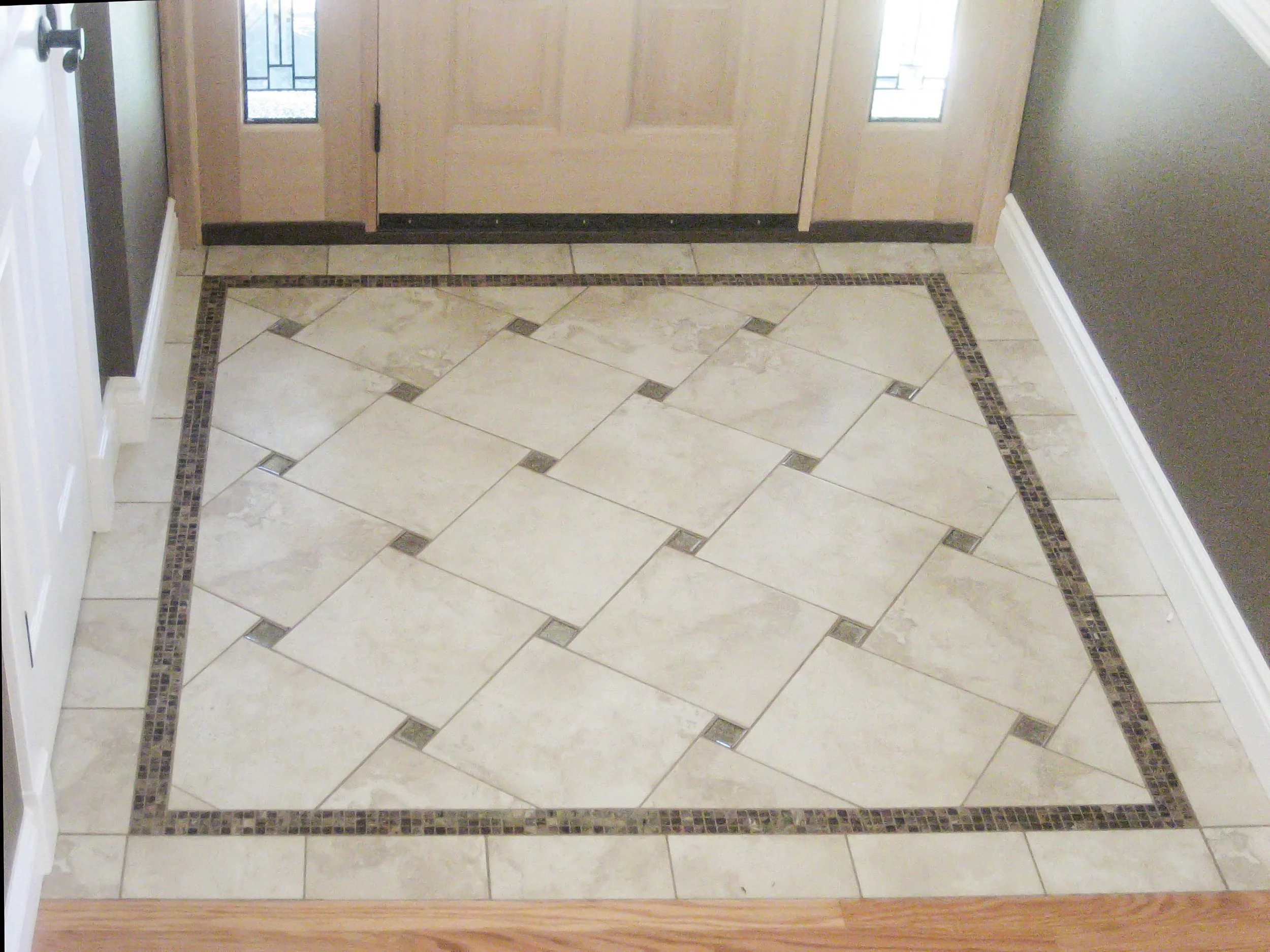 Decorative tiled floor with a border pattern and a wooden threshold, leading to a door with glass panels.