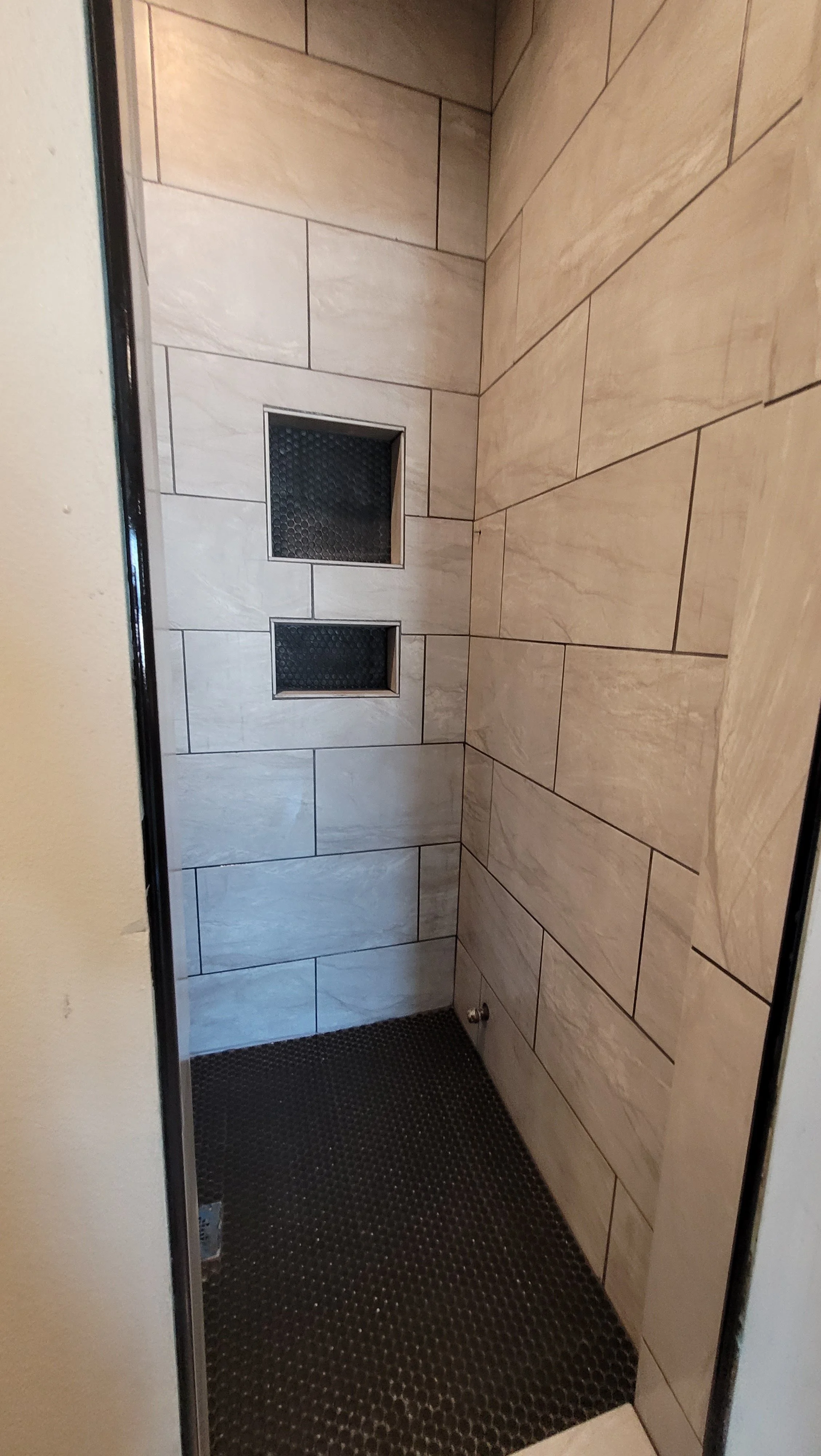 Luxury walk-in shower featuring beige ceramic wall tile and black penny round mosaic floor