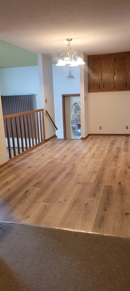Empty living space with wood flooring, a chandelier hanging from the ceiling, a staircase with a wooden handrail, and a front door with an oval glass window.