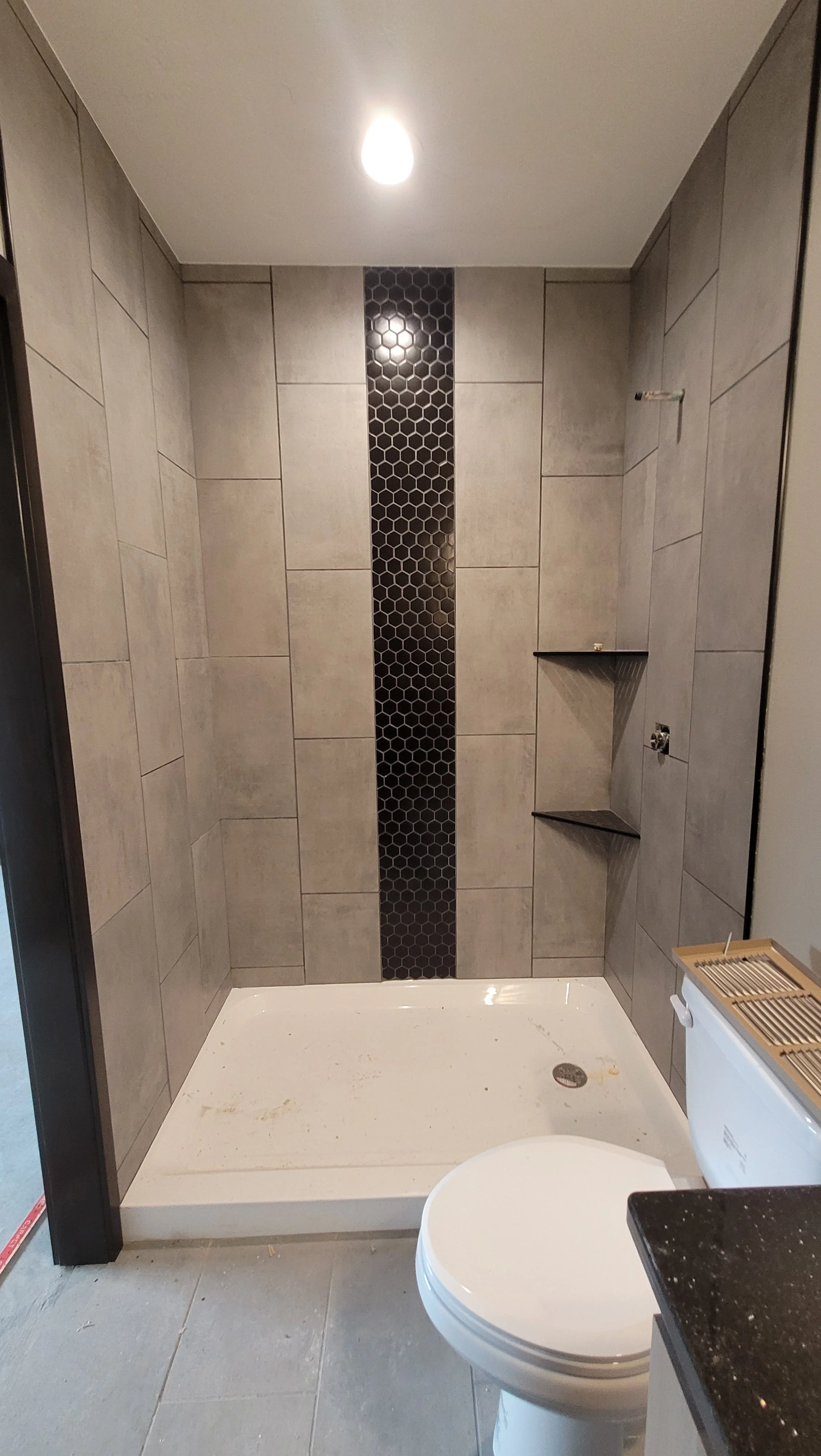 Contemporary walk-in shower with large beige ceramic tiles and dark mosaic accent wall
