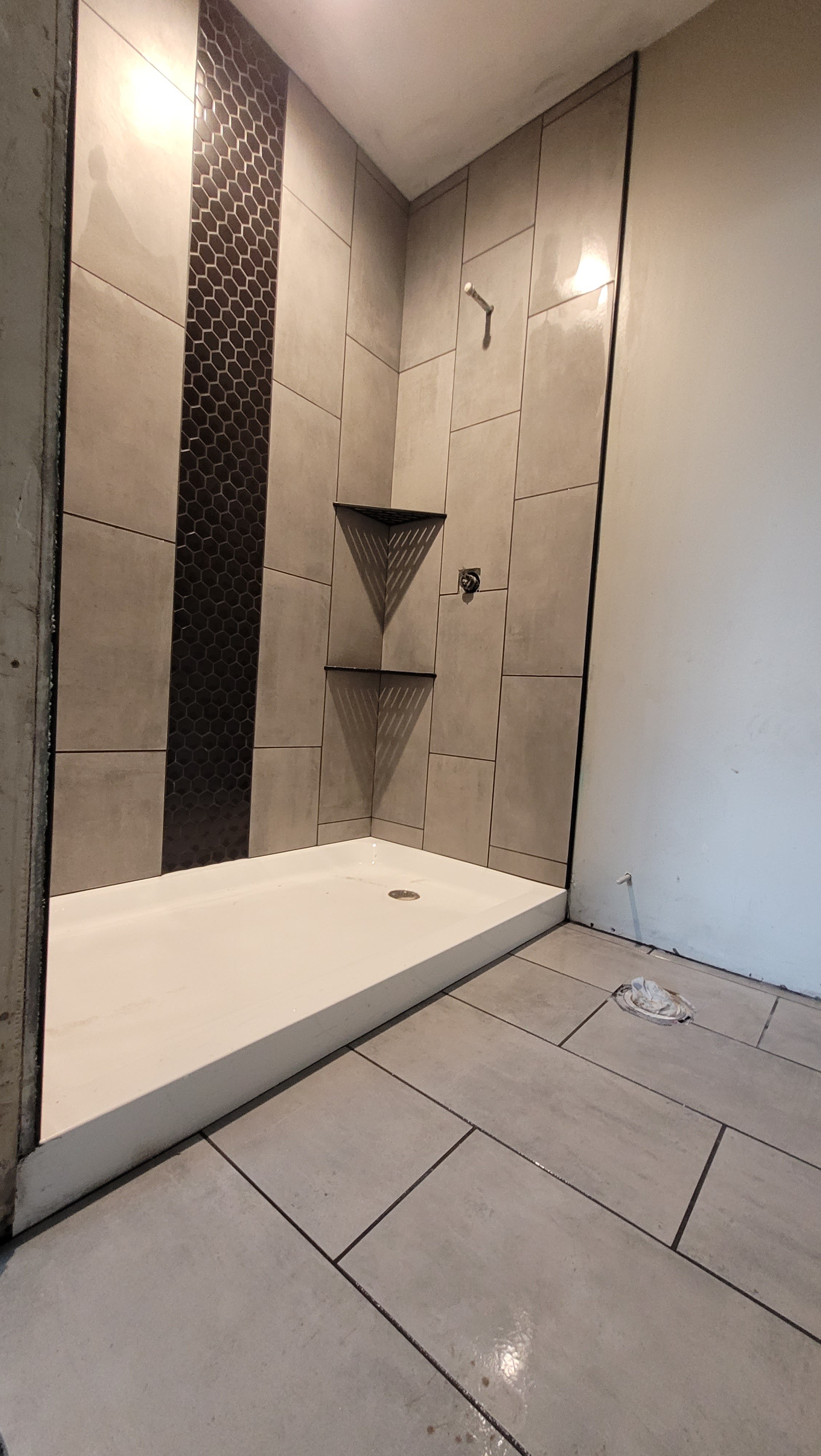 New construction shower pan with light gray ceramic tile flooring installation