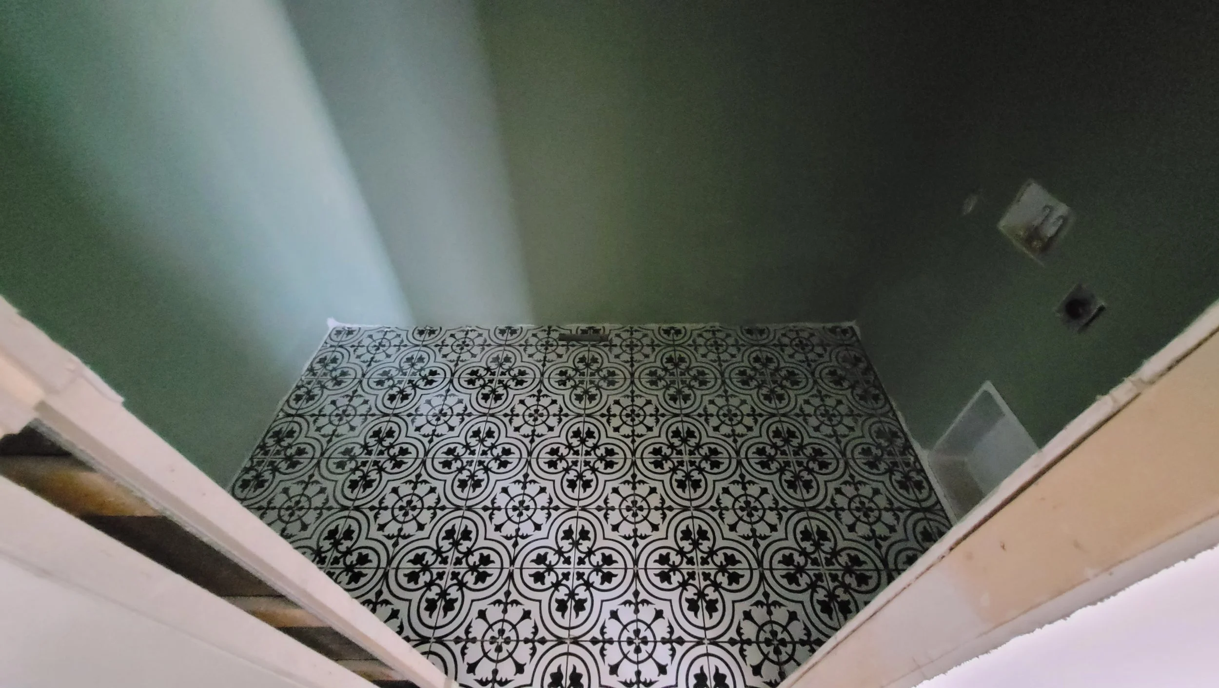 Black and white patterned ceramic tile floor installation in progress with green painted walls