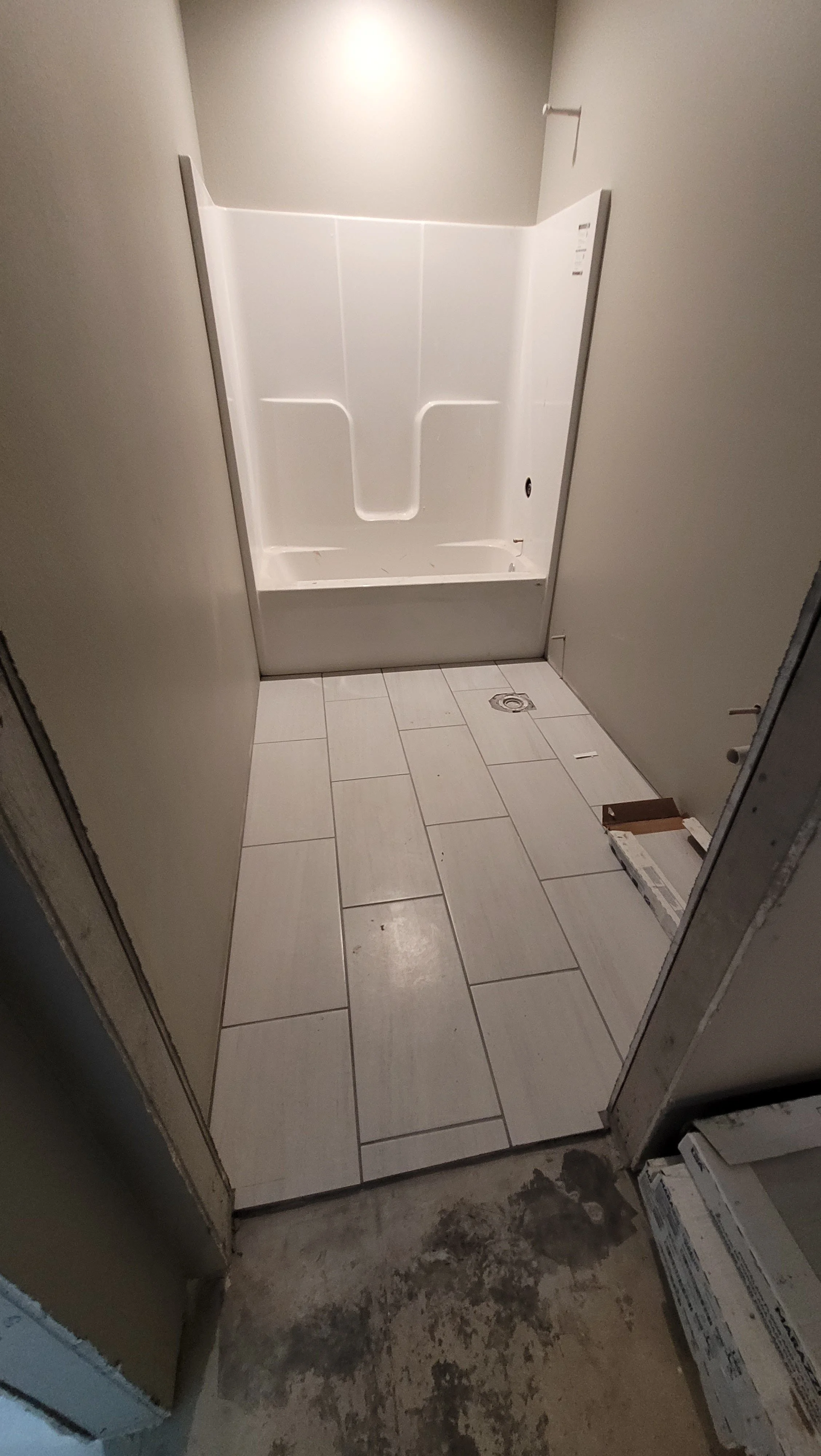 Empty shower stall with white surround, beige walls, beige floor tiles, and construction materials around the doorway.